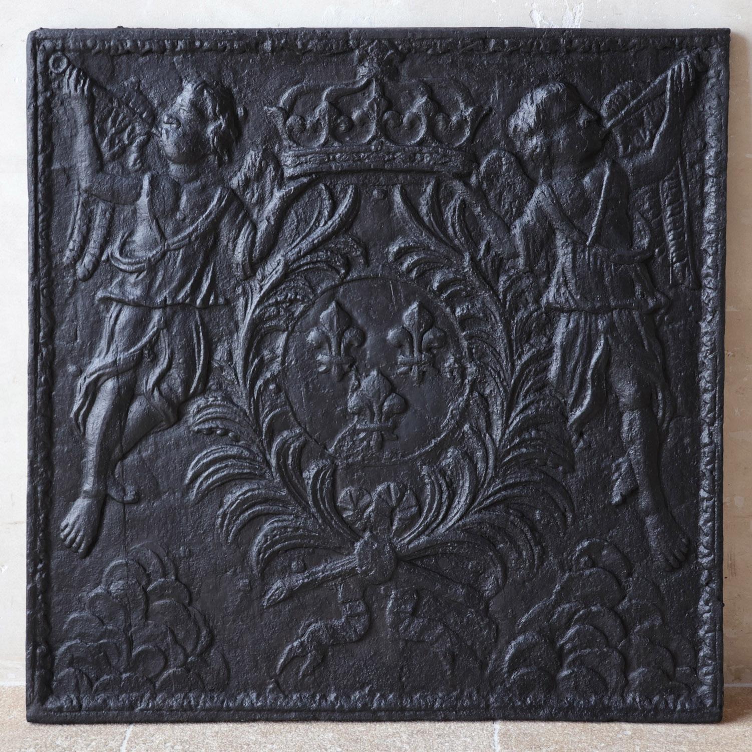 Très grande plaque de cheminée en fonte du XVIIIe siècle. Deux anges volants et trompettistes tiennent un blason royalement couronné et orné de trois fleurs de lys, symbole de la cour royale française.

Dimensions : 97 cm de haut x 97 cm de large :