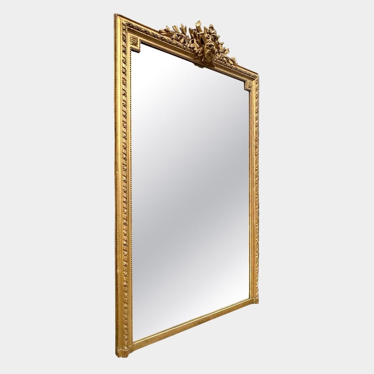 Un grand miroir ancien de style Louis XVI. Le cadre est décoré d'un ruban torsadé et d'un motif floral, le feuillet intérieur est perlé.
Rosettes dans les coins des épaules. Le cartouche central représentant une feuille de laurier, une partition et
