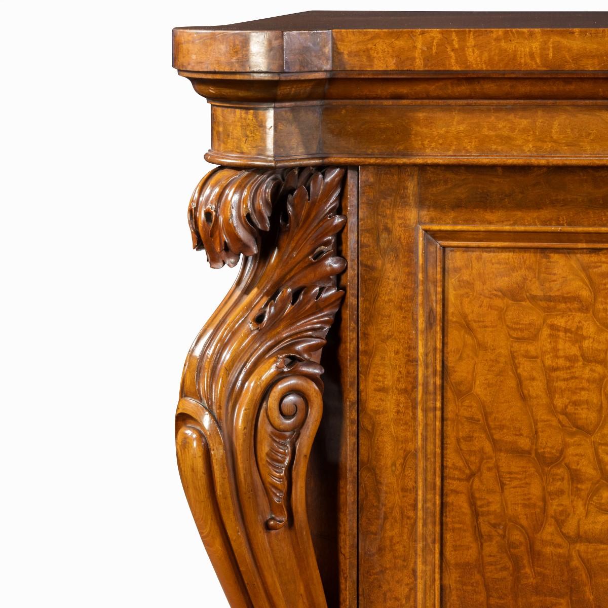 A very large George IV plum pudding mahogany side cabinet, the shaped top above a moulded frieze with five cupboard doors interspersed between scrolling acanthus columns, the three central doors glazed with pleated fabric linings opening to reveal a