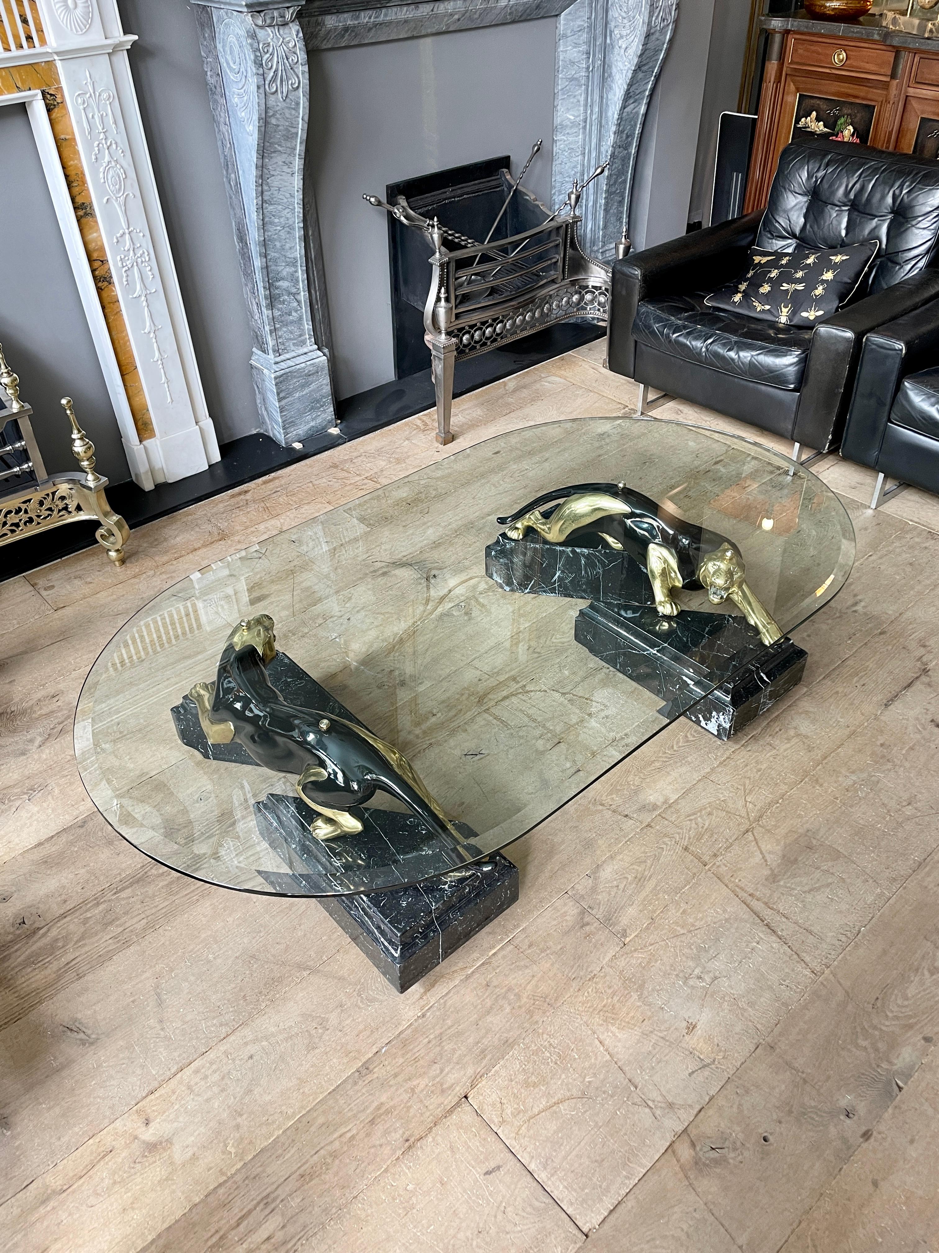 A very large cocktail or coffee table with triangular stepped Nero Marquina marble bases supporting two ebonized and brass panthers, all underneath a shaped and bevelled thick glass top. A striking and avant garde table very much of the 70's Italian