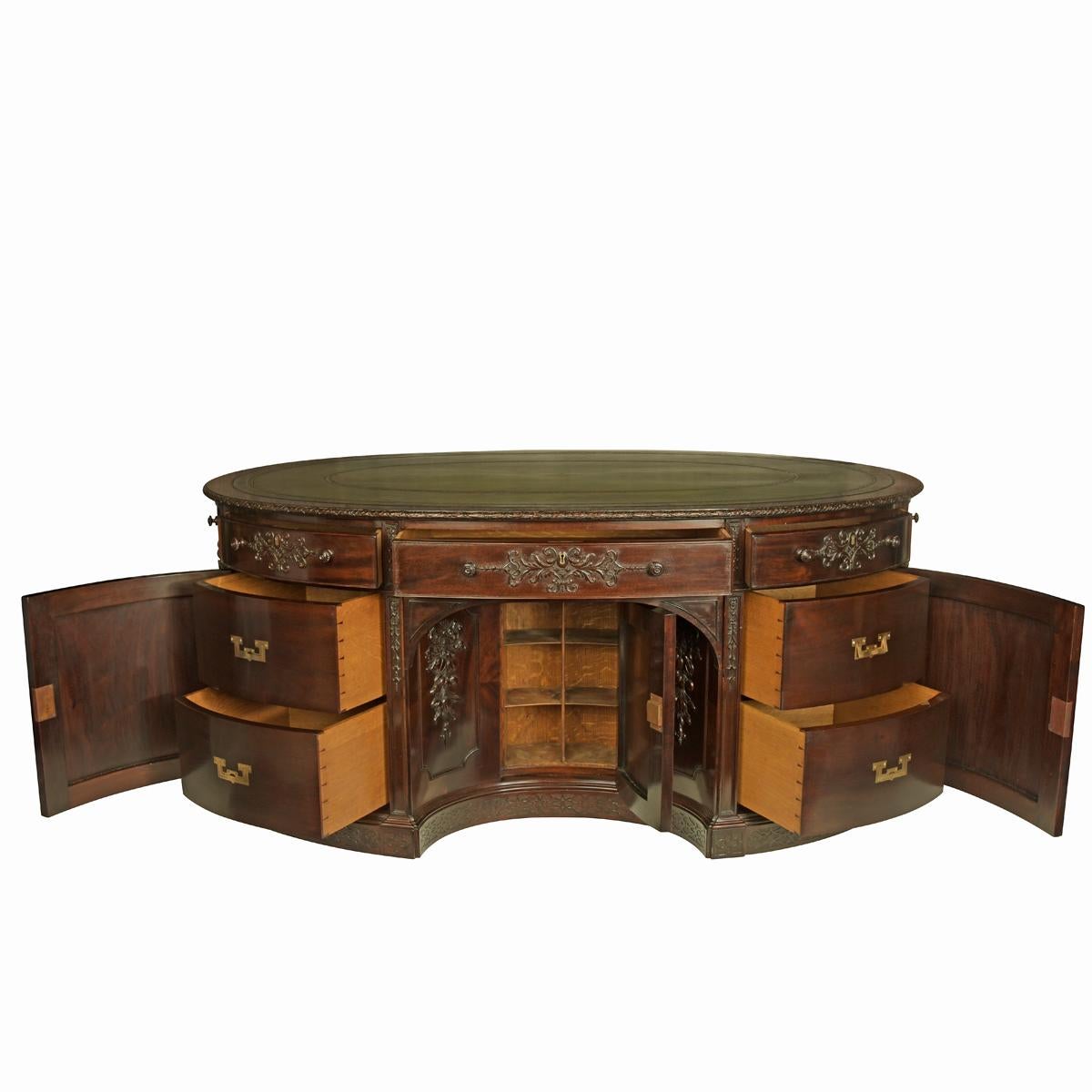 A very large mahogany centrepiece partners’ desk in the Chippendale style, attributed to Maples or Gillows, of oval form with a replaced green leather top, the frieze with six small and two dummy drawers, each side with a kneehole containing a