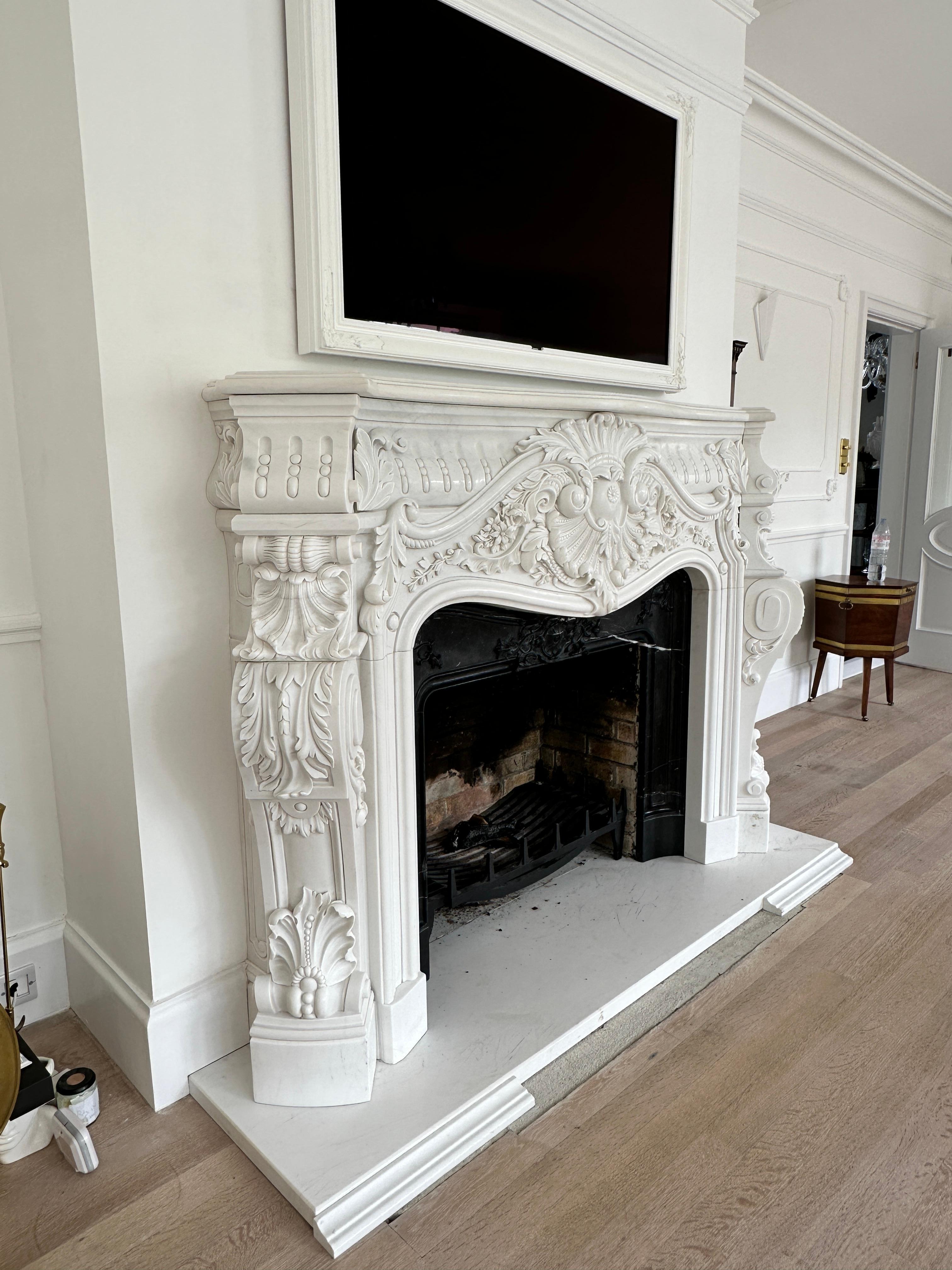 A very large reclaimed French Rococo style fireplace in white marble. The profusely carved jambs with scrolls, shells and acanthus supporting a wide serpentine equally carved frieze with a very large central cartouche. Scrolled endblocks with fluted
