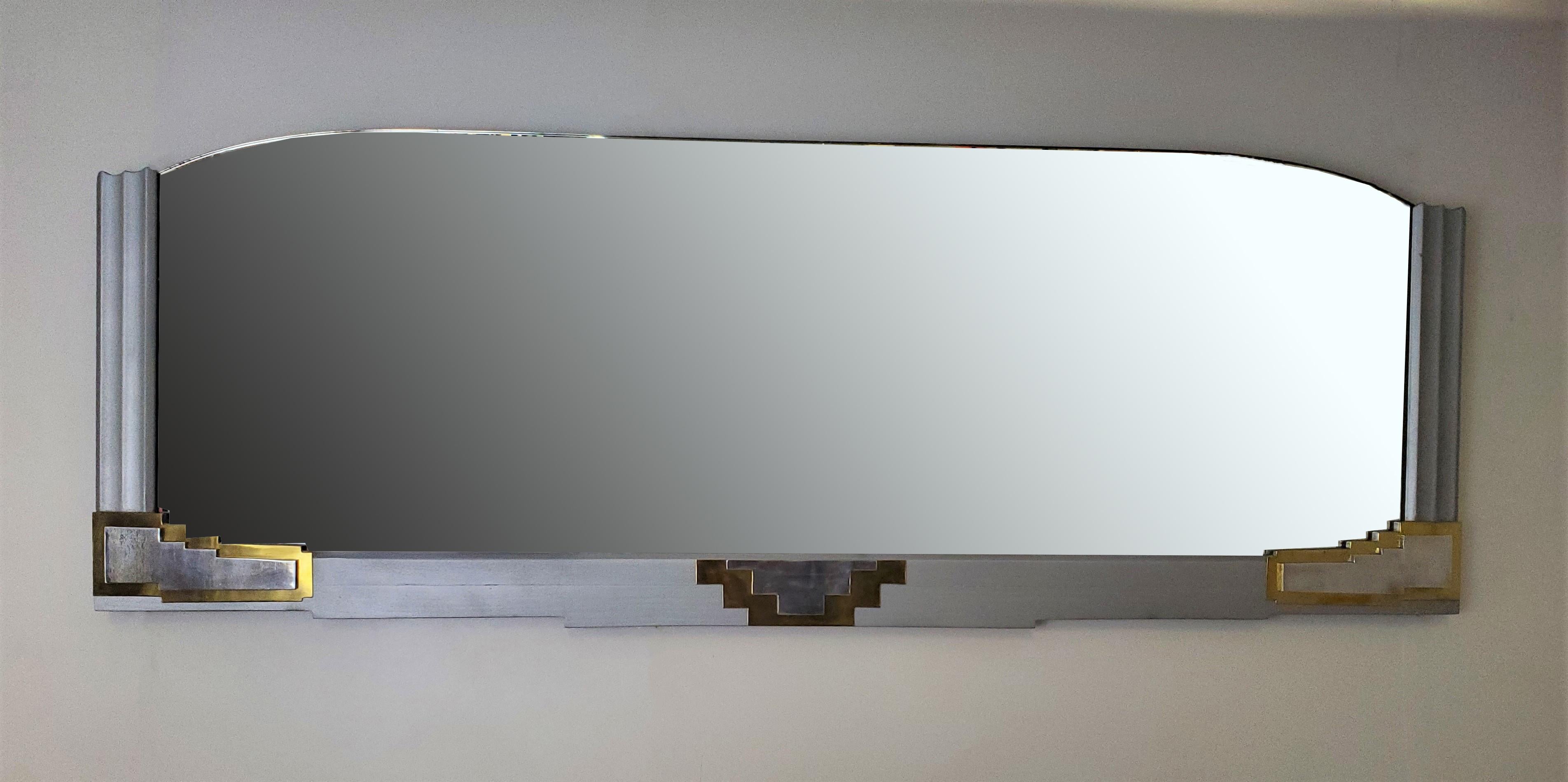 An original French Art Deco long, wide and rectangular, silver over wood 
wall mirror with slightly curved top, fluted sides and angular accents of nickel and brass.
The highly decorative ziggurat, sky scraper, stylized representation on the