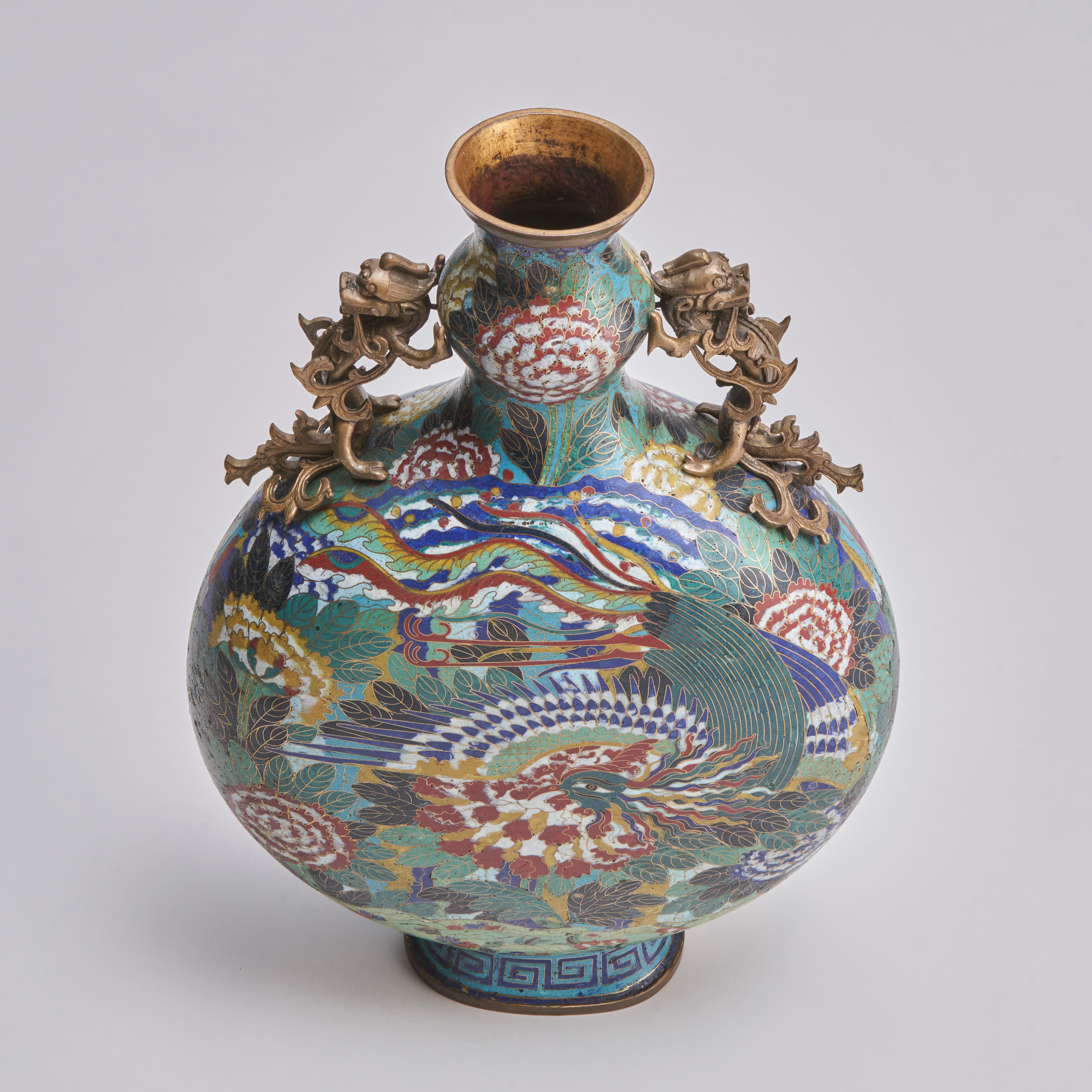 A 19th century Chinese cloisonne moon flask (Baoyueping) with bright polychrome decoration of a phoenix flying among large peonies, twin brass fo dogs flank the top and the foot is decorated with a meandering line.

Contact us for further images or