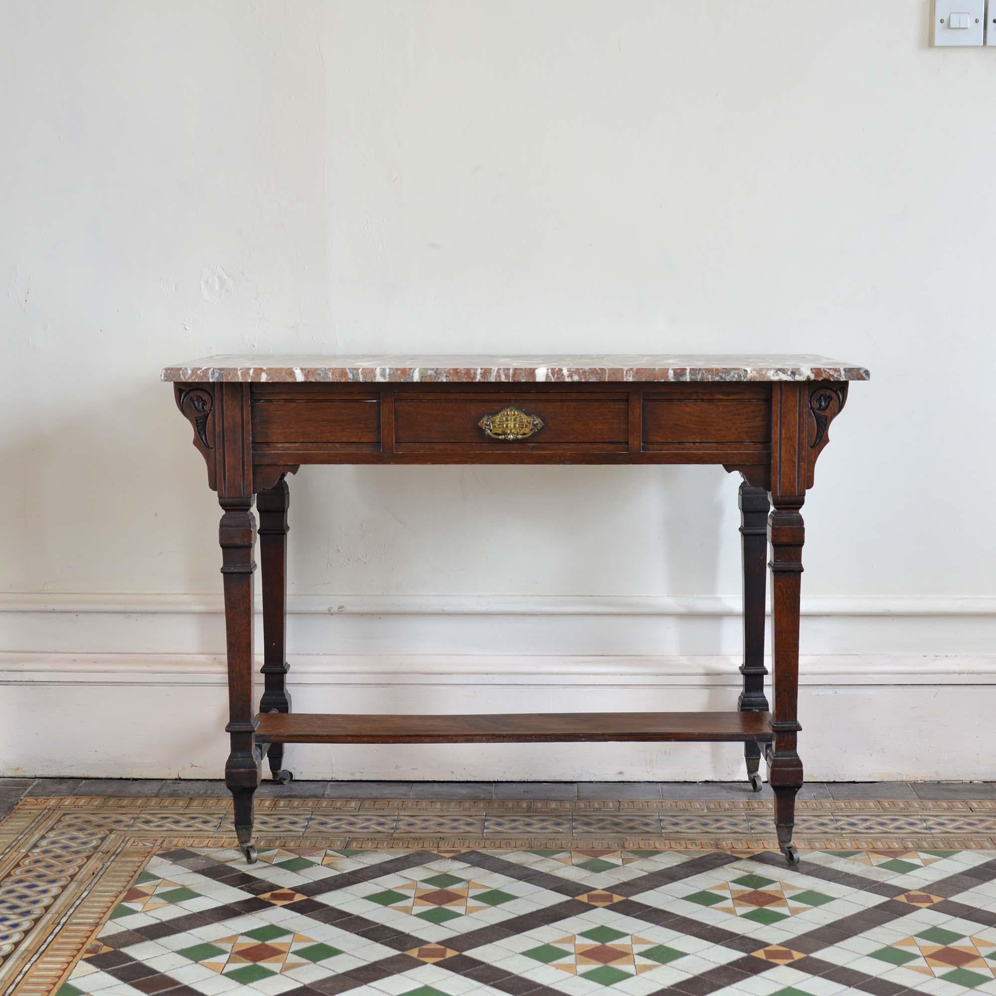 A Victorian Aesthetic Movement marble topped table
The Rosso Bilbao red marble top with square cut corners and chamfered edge.  The oak base of typical Aesthetic styling, the frieze with one central drawer and stylised wings to each end, stands on