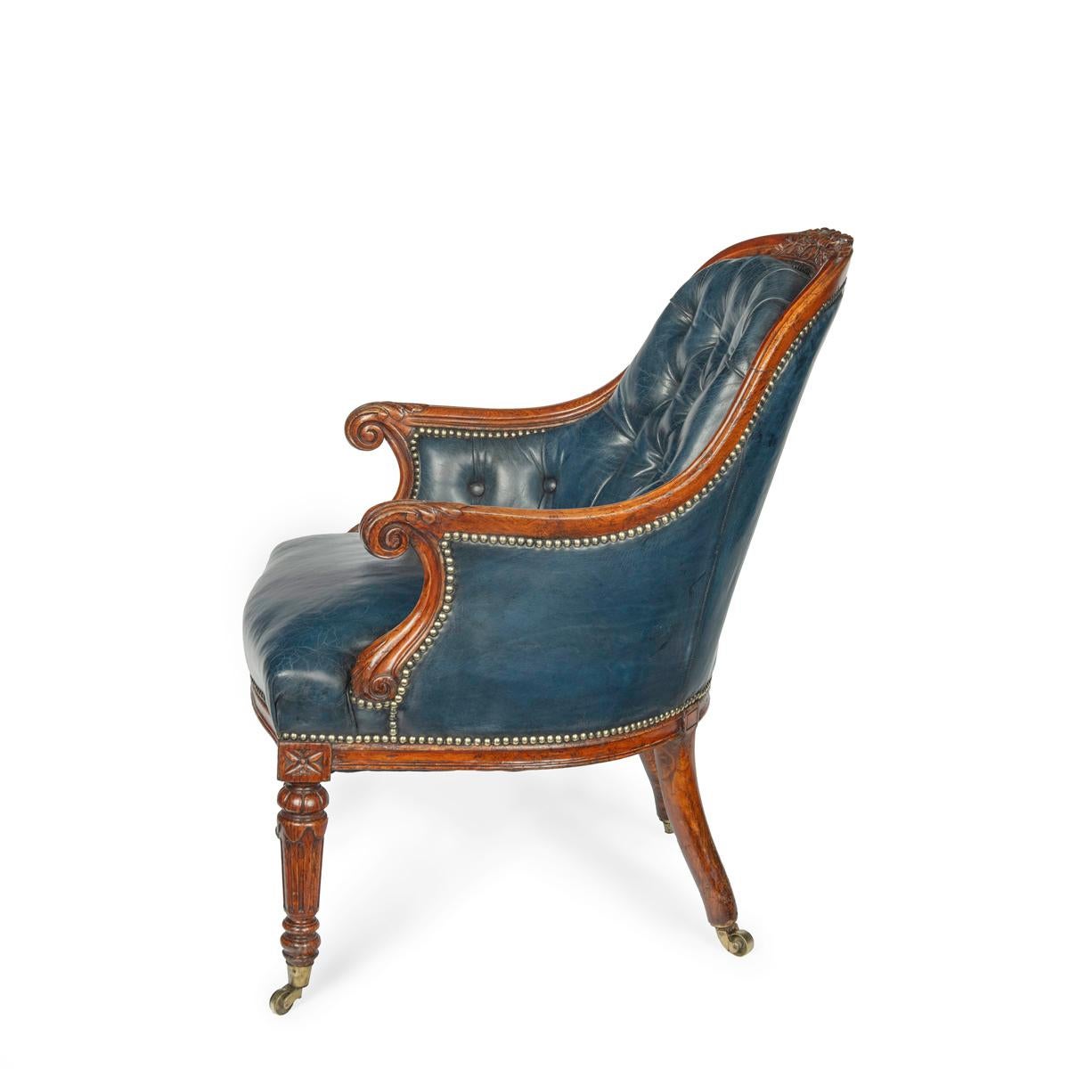 A Victorian blue leather oak library chair, the arched back continuous with the scroll arms, and carved with beribboned foliate sprays in the centre, the shaped seat rail set above turned, reeded tapering legs, original brass castors. Re-upholstered