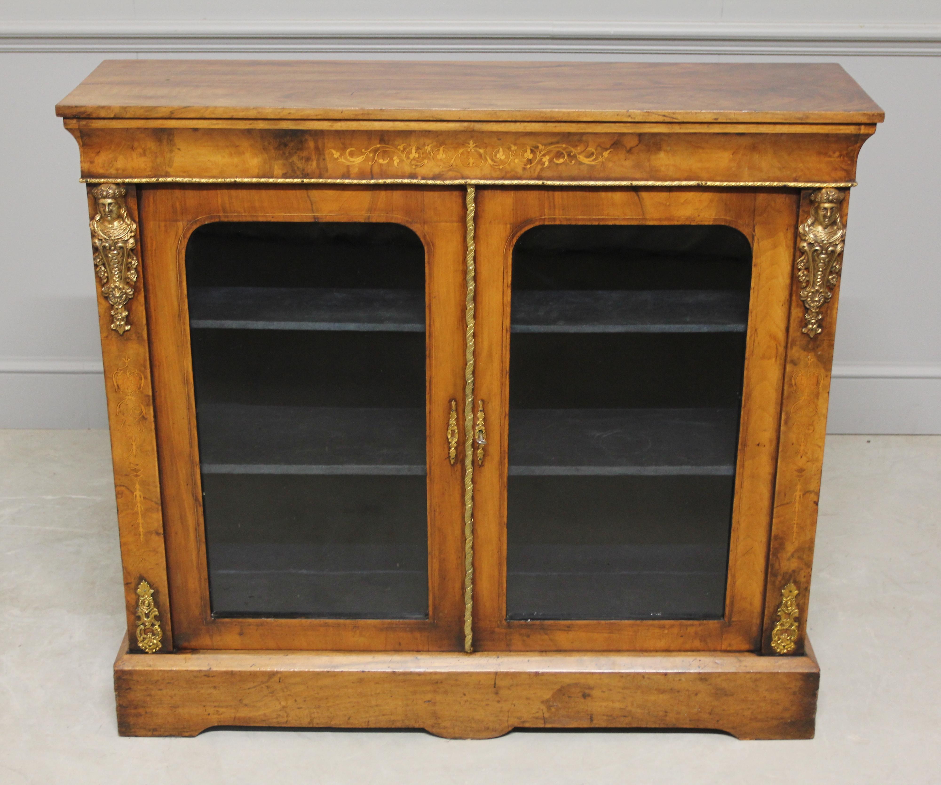 A Victorian burr walnut two door display cabinet with ormolu mounts and satinwood Arabesque inlay on a shaped plinth base, with working key and lock.
Measures: H 104cms W 114cms x D 32cms 
Coming from the Queen Victoria period is burr walnut