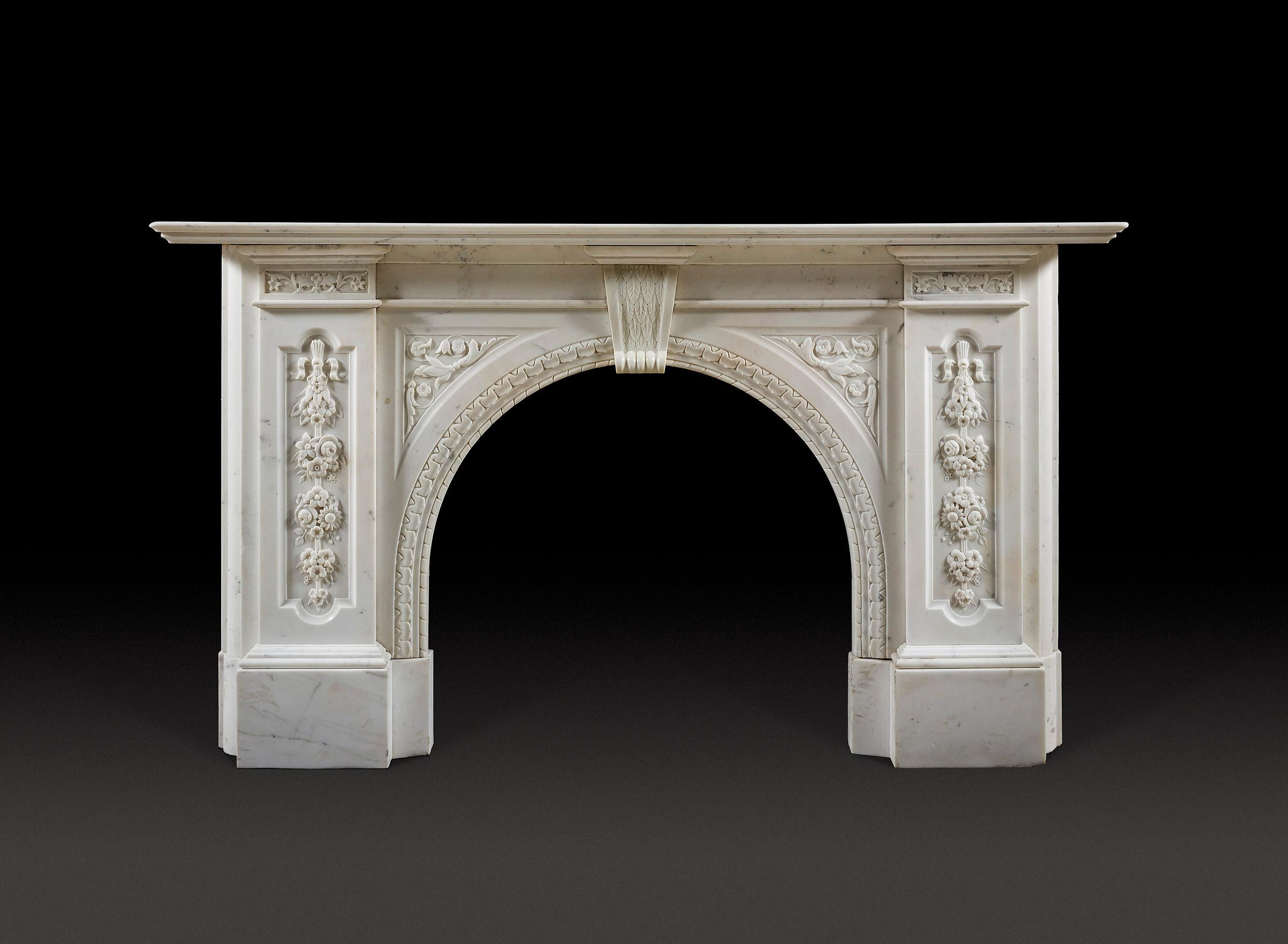 Une cheminée en marbre de Carrare de la fin de l'époque victorienne avec une ouverture moulée en arc, surmontée d'une clé de voûte en encorbellement flanquée d'écoinçons feuillagés. Les lourds jambages sont ornés de losanges cintrés sculptés de