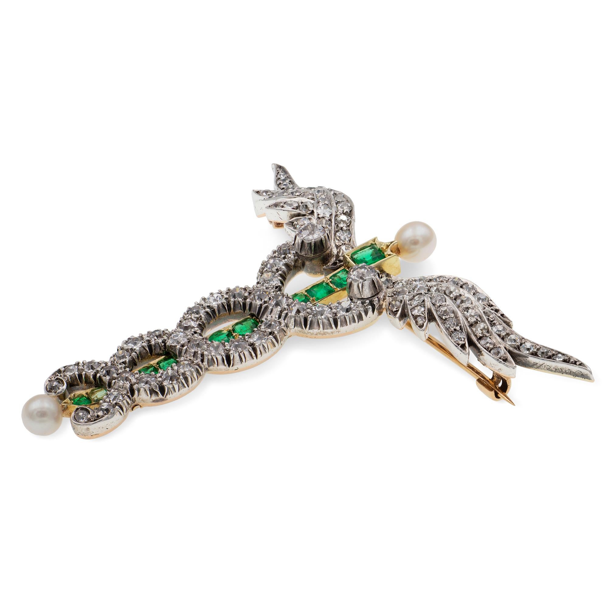 A Victorian diamond, emerald and pearl caduceus brooch, the staff set with ten faceted emeralds estimated to weigh a total of 0.8 carats mounted in 18ct yellow gold, terminating to a round pearl on each end, the entwined serpents and the wings