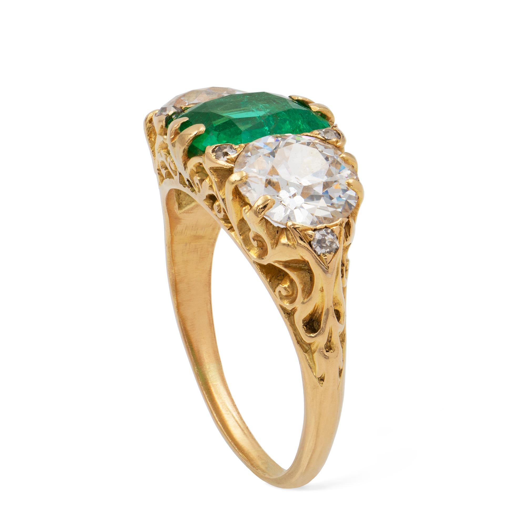 A Victorian emerald and diamond three-stone ring, the cushion-shape faceted emerald, weighing 1.88 carats, set between two round old European-cut diamonds weighing 2.30 carats in total, all claw-set with old-cut diamonds in-between, to a gold mount