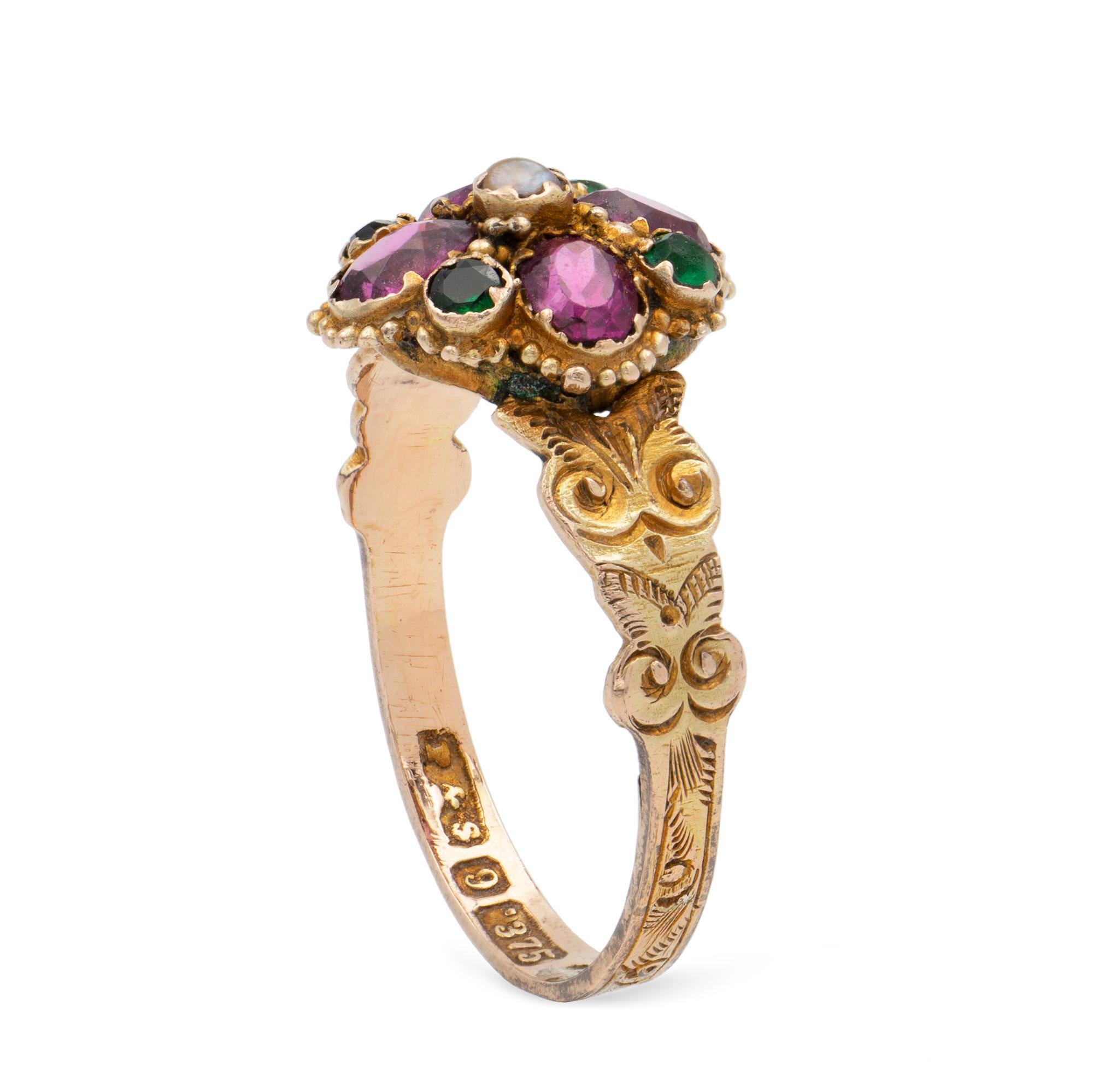 A Victorian garnet and emerald ring, to the centre a seed pearl surrounded by four oval faceted purple garnets, flanked with four round emeralds, all rub-over set to a yellow gold shank engraved with scroll and foliate decorations, marked 9ct gold,