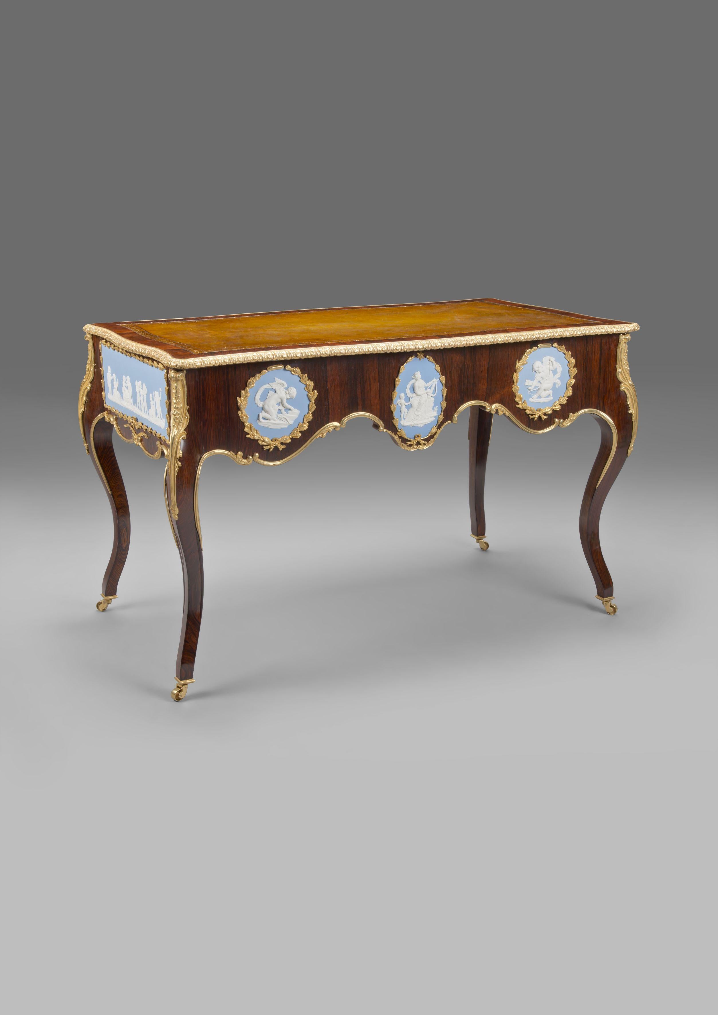 A Victorian gilt-bronze and Jasper-Ware mounted writing table. 

English, circa 1860. 

This fine bureau plat or side table has a leather top with a Greek key gilt border above a shaped apron to the front mounted with Wedgwood style jasper-ware