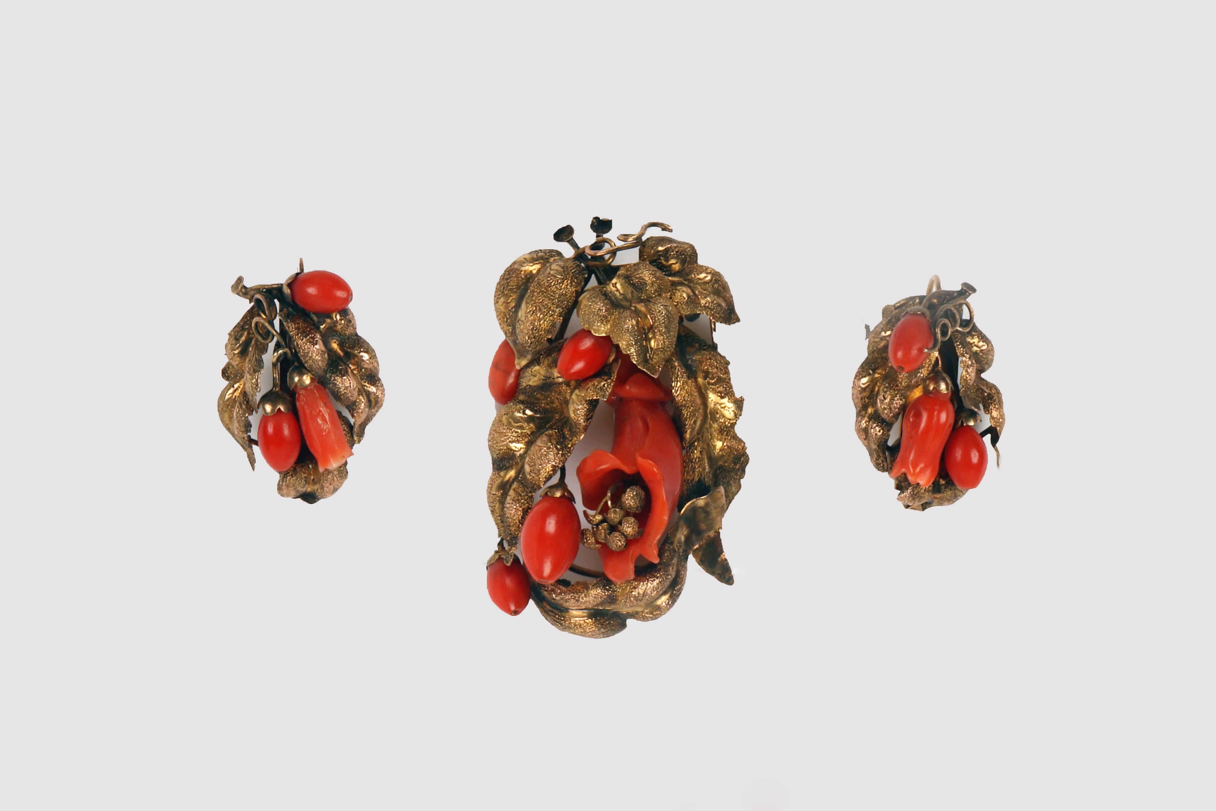 Set of pendant earrings and brooch in 14 Kt gold and coral. The set consists of three pieces, a brooch and a pair of simple hook earrings. The earrings reproduce similar but not identical designs. Made with gold casting, embossing, chasing and burin