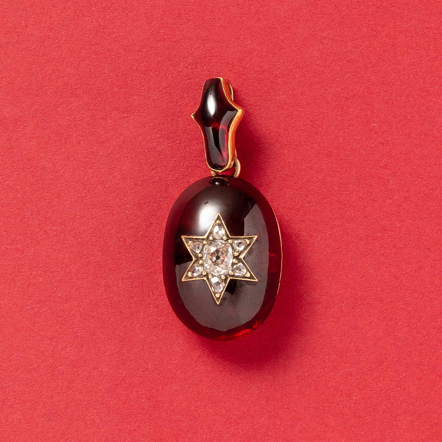 A 15 carat gold Victorian oval pendant set with a large deep red carbuncle garnet incrusted with a six pointed star at the centre set with a large cushion cut diamond surrounded by six rose cuts diamonds. The bail is also set with a matching garnet,