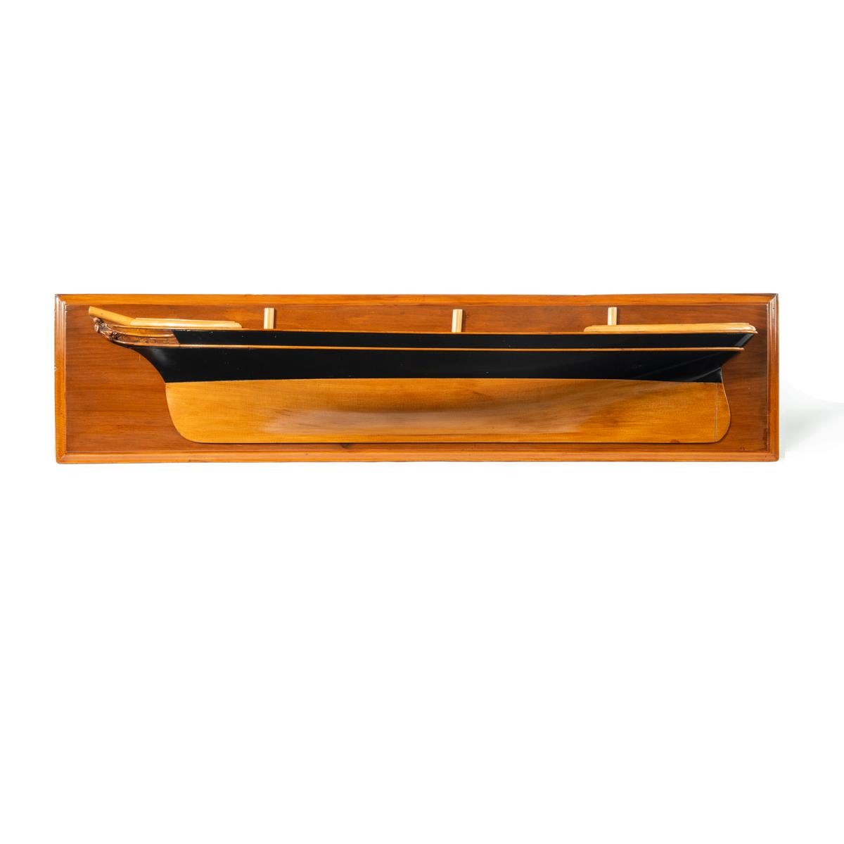 Modèle victorien de demi-coque d'une goélette anglaise à trois mâts, représentée face à la gauche, la coque en bois souple façonnée avec des côtés supérieurs peints en noir et des rambardes et des plats-bords en bois appliqués, la proue avec des