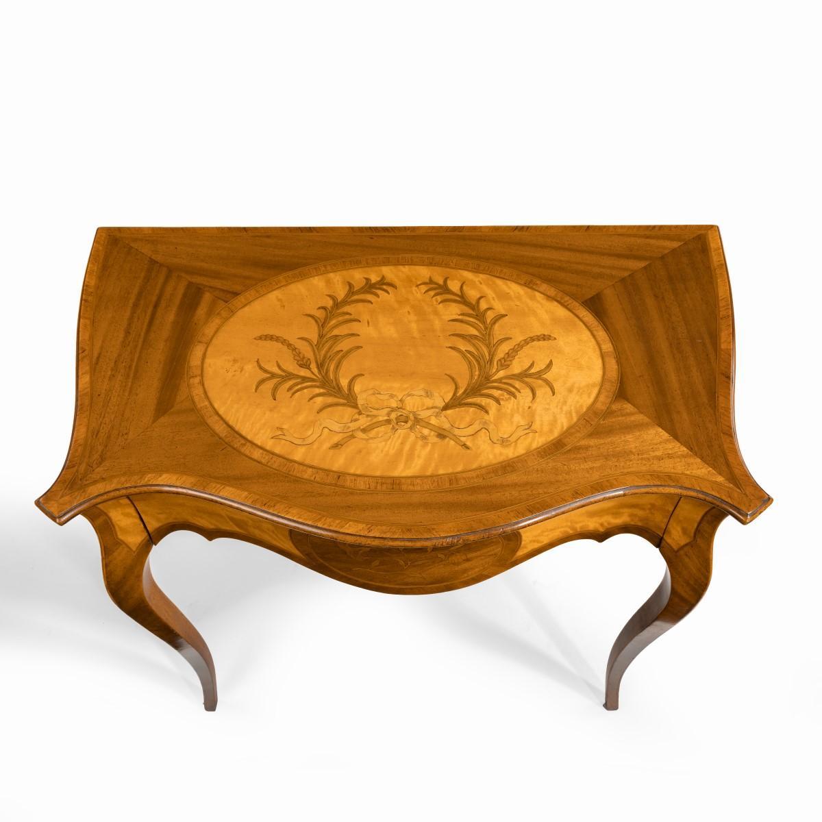 A Victorian inlaid satinwood and kingwood table in the style of Hepplewhite, the serpentine top above a single disguised frieze drawer raised on slender shaped legs, the top decorated with an oval panel inlaid with a laurel wreath on a satinwood