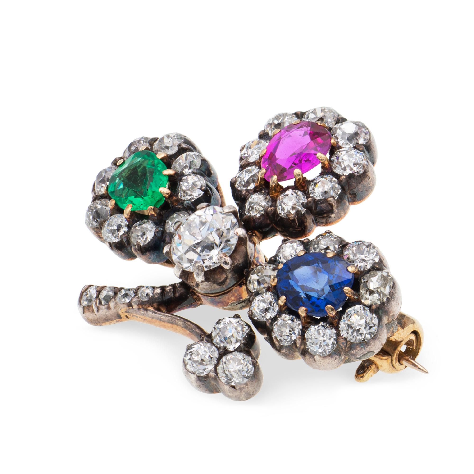 Eine viktorianische Kleeblatt-Brosche mit mehrfarbigen Edelsteinen und Diamanten, die drei Blätter sind jeweils mit einem birnenförmigen Stein, einem Smaragd, einem Rubin und einem Saphir besetzt, jedes umgeben von neun Diamanten im alten