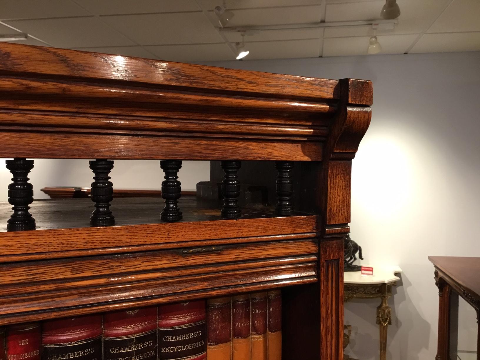 A Victorian Period oak Gothic Revival open bookcase. With an ebony turned balustrade top and slightly projecting solid oak ends above four adjustable shelves, each shelf with a hinged dust flap. Supported on projecting sledge feet and with solid oak