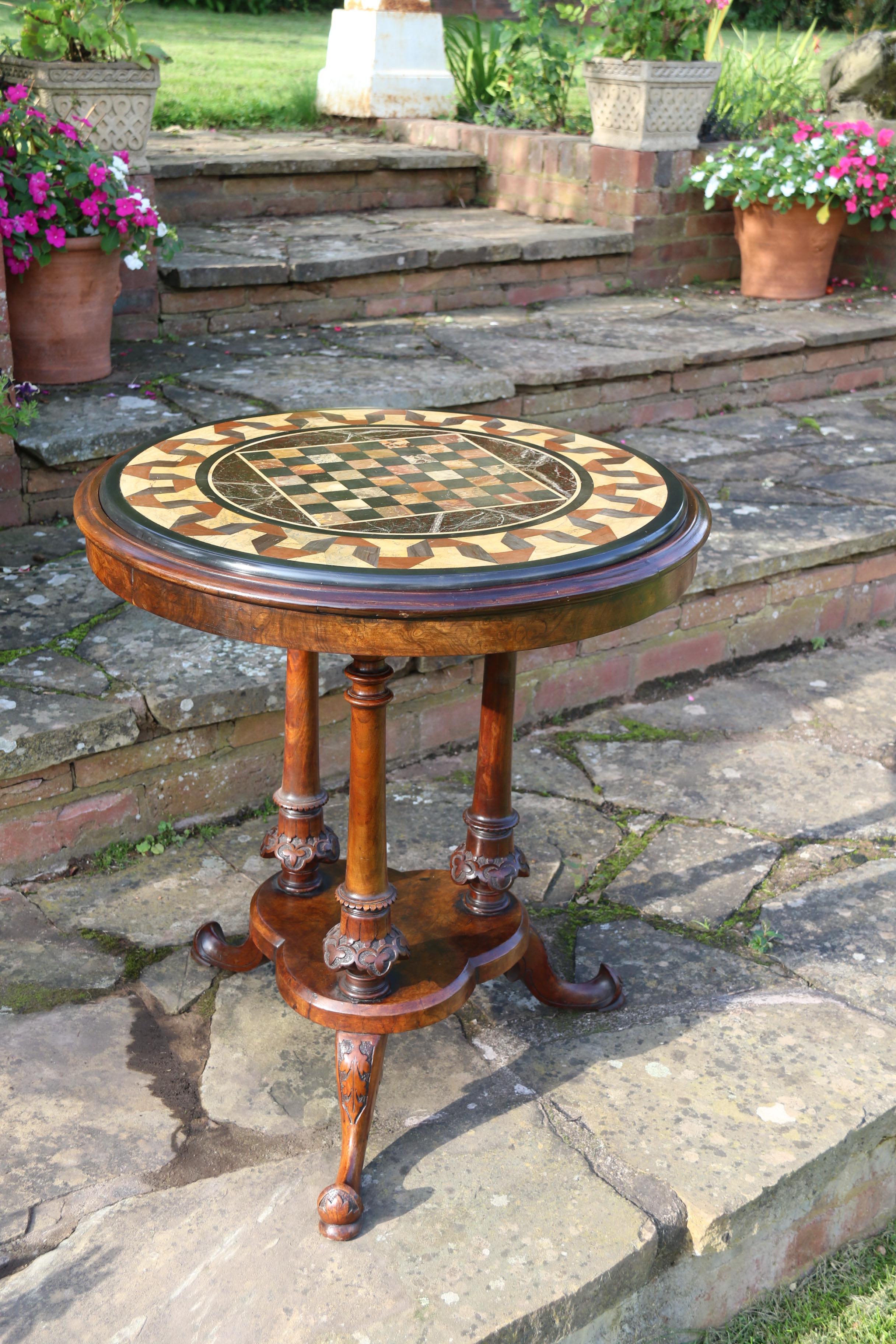 This a very beautiful Victorian pietra dura and burr walnut occasional/games table. The table stands on three shaped and foliate carved legs which support a clover leaf shaped platform with three turned and foliate carved columns rising up to a