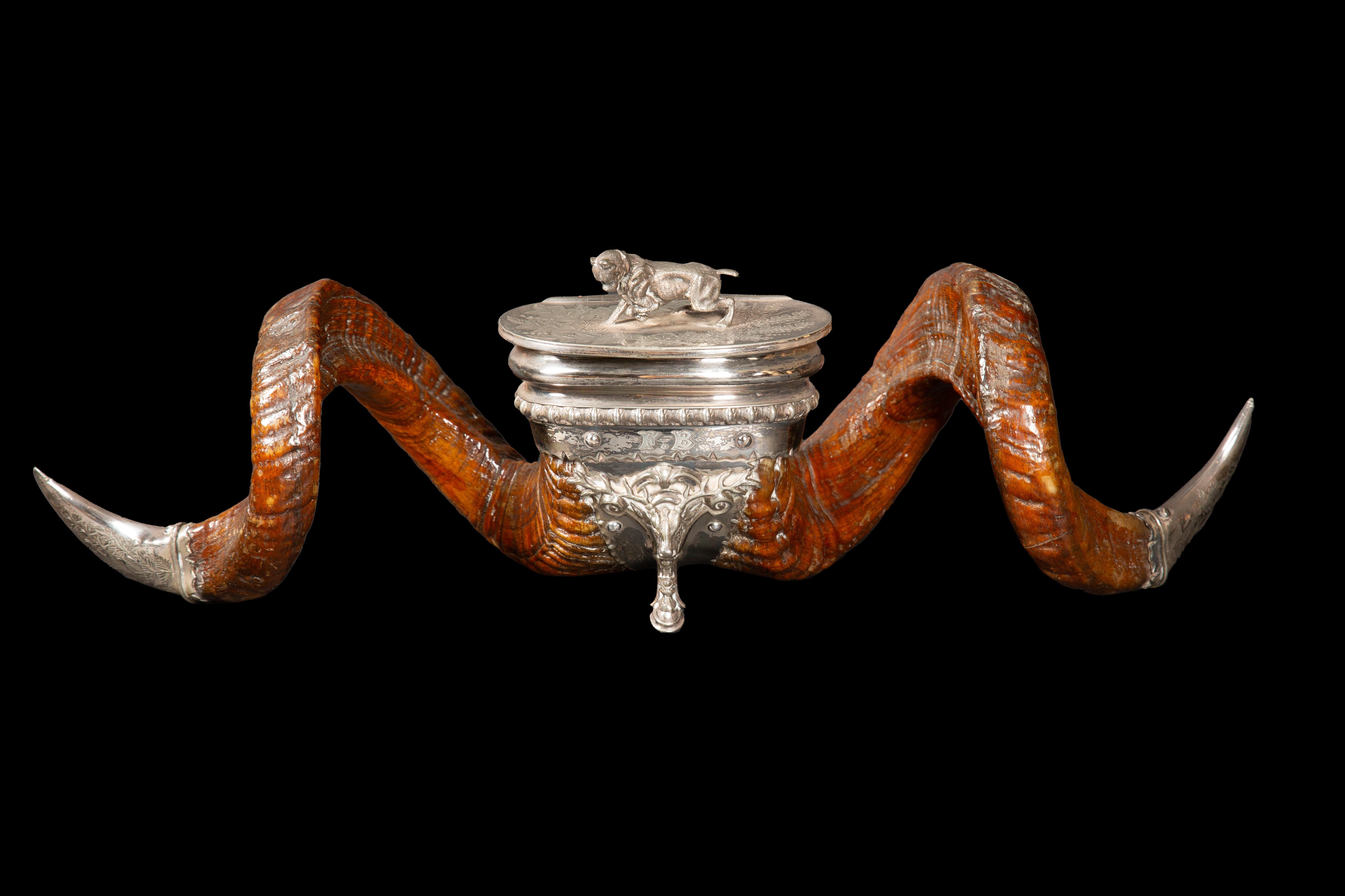A VICTORIAN RAM'S HORN SNUFF MULL WITH ELECTROPLATED MOUNTS 
MARK OF WALKER & HALL OF SHEFFIELD, CIRCA 1880 
Cover surmounted by a boxer dog and engraved with ferns, on a stag's head and hoof support, the horns tipped with claw-shaped mounts
2 in.