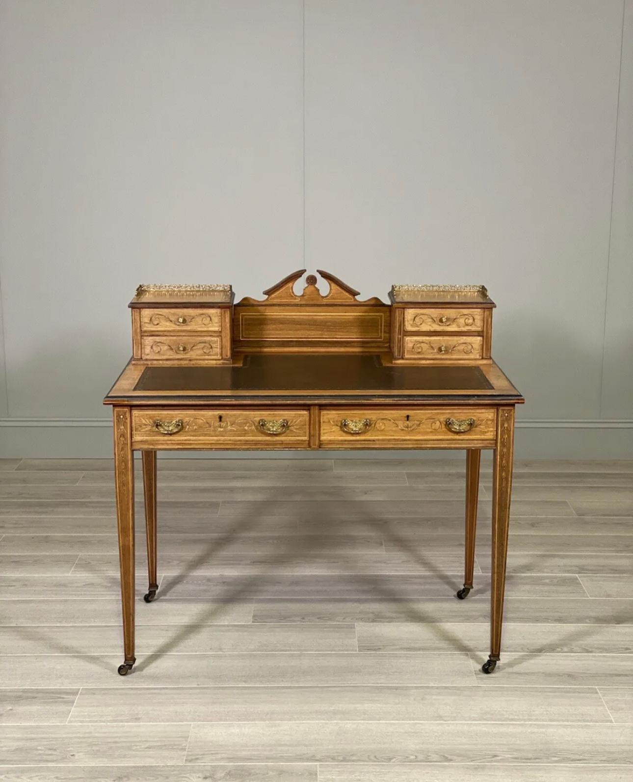 A fine quality desk made by the famous furniture maker Maple & Co. The desk has decorative inlayed rosewood veneers, four desktop drawers with brass galleries, two large drawers, original leather writing surface and site on tapered inlaid legs with