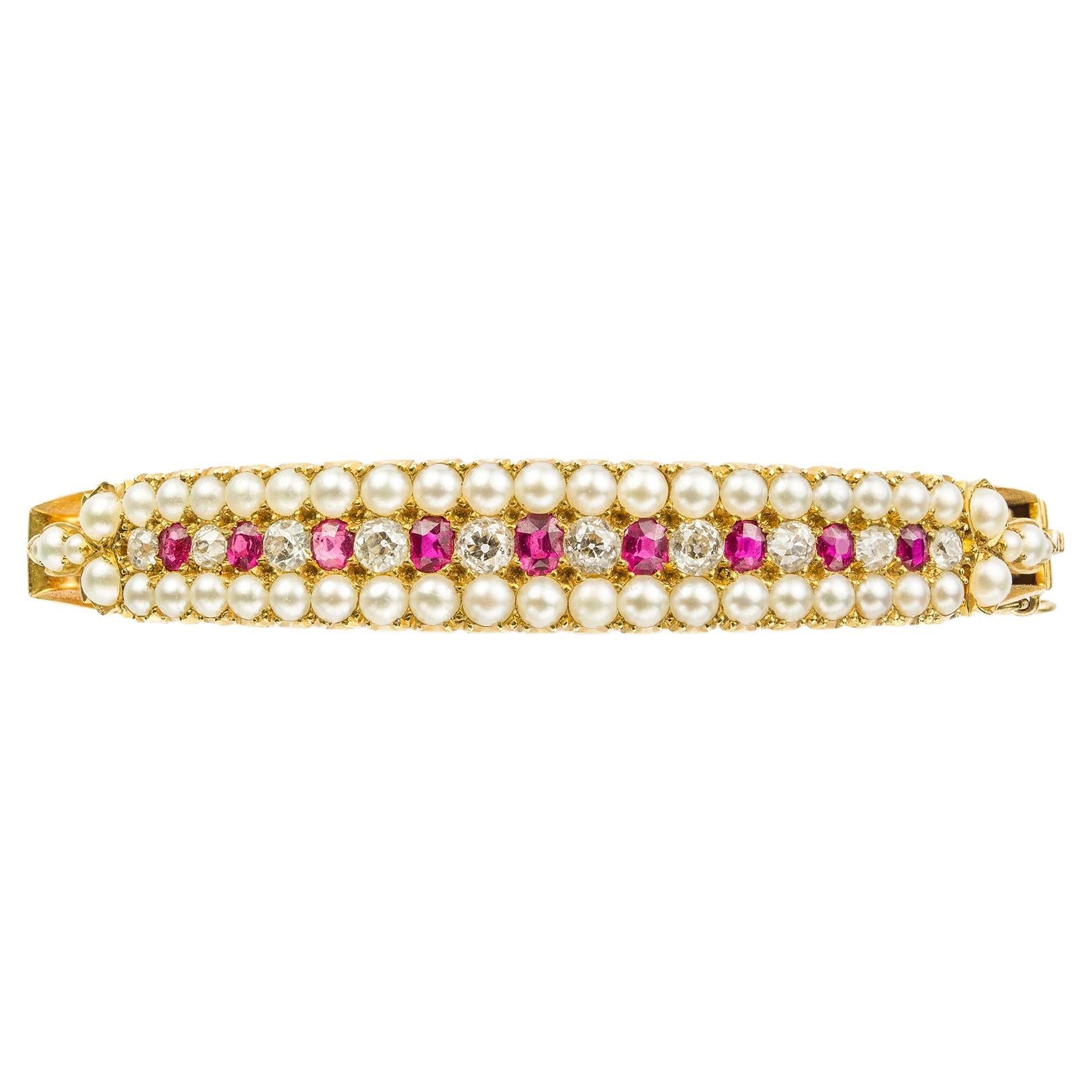 A Victorian pearl, ruby and diamond bangle, consisted of three rows, the central one set with ten  old brilliant-cut diamonds graduating from the centre, alternating-set with nine oval faceted rubies, the two outer rows set with nineteen seed pearls