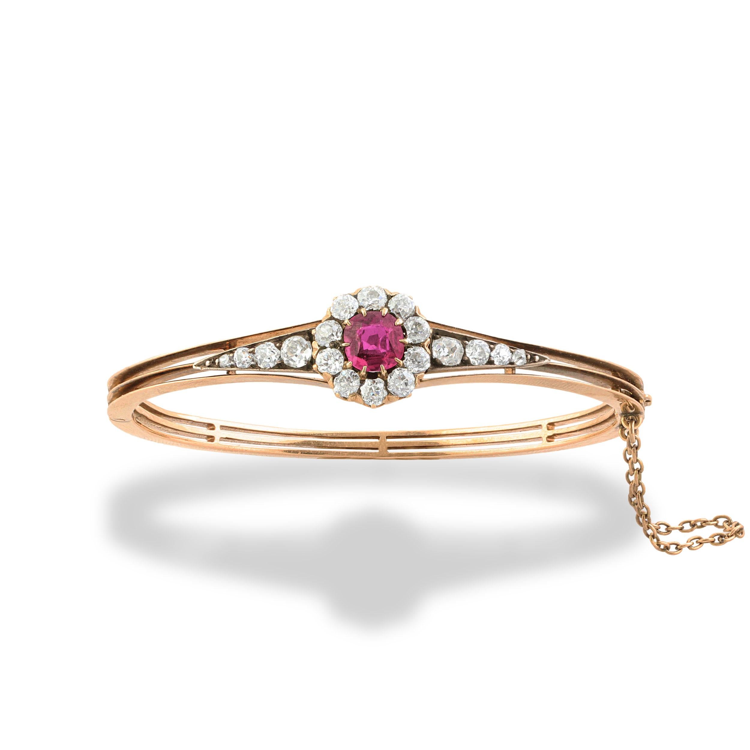 A Victorian ruby and diamond hinged bangle. Set at the centre with a cushion-cut ruby amongst a cluster of old-cut diamonds framed with a graduated line of diamonds. Mounted in silver on gold. Ruby weight = 1.20 carats.