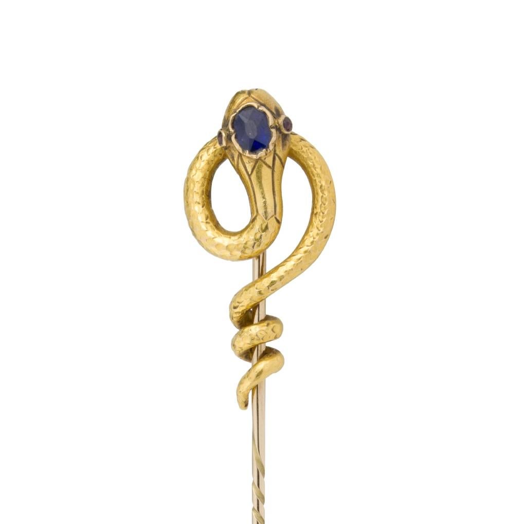 A Victorian snake pin, the head set with a sapphire and ruby eyes, the tapering embellished tail entwined around the stick pin, 18ct yellow gold, circa 1880, the jewelled part measuring approximately 32 x 15mm, the pin measuring 8cm long, gross