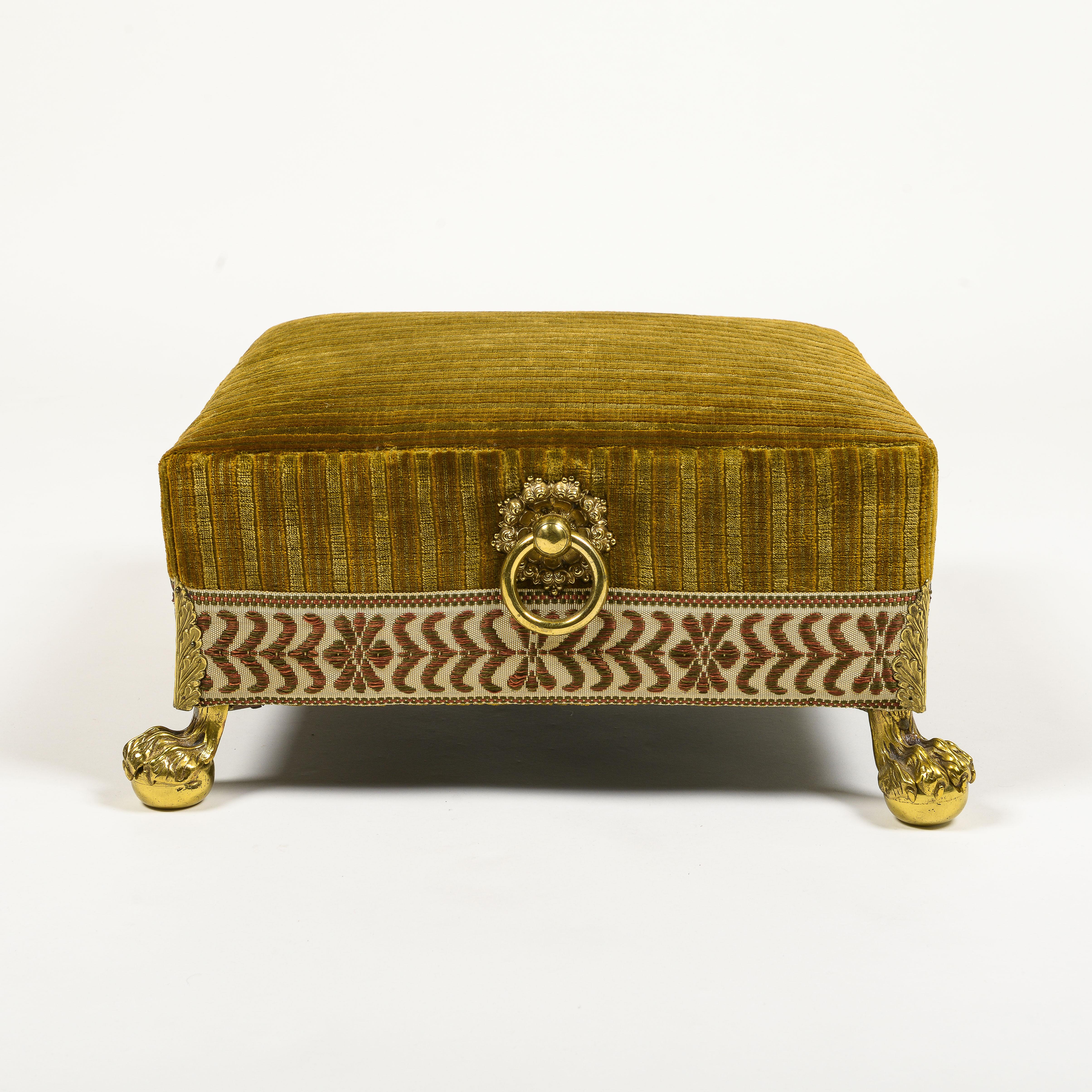 Covered in a gold linen velvet finished with a broad silk tape; mounted with brass carrying handles to the sides and raised on brass hairy paw feet issuing foliate sprays.