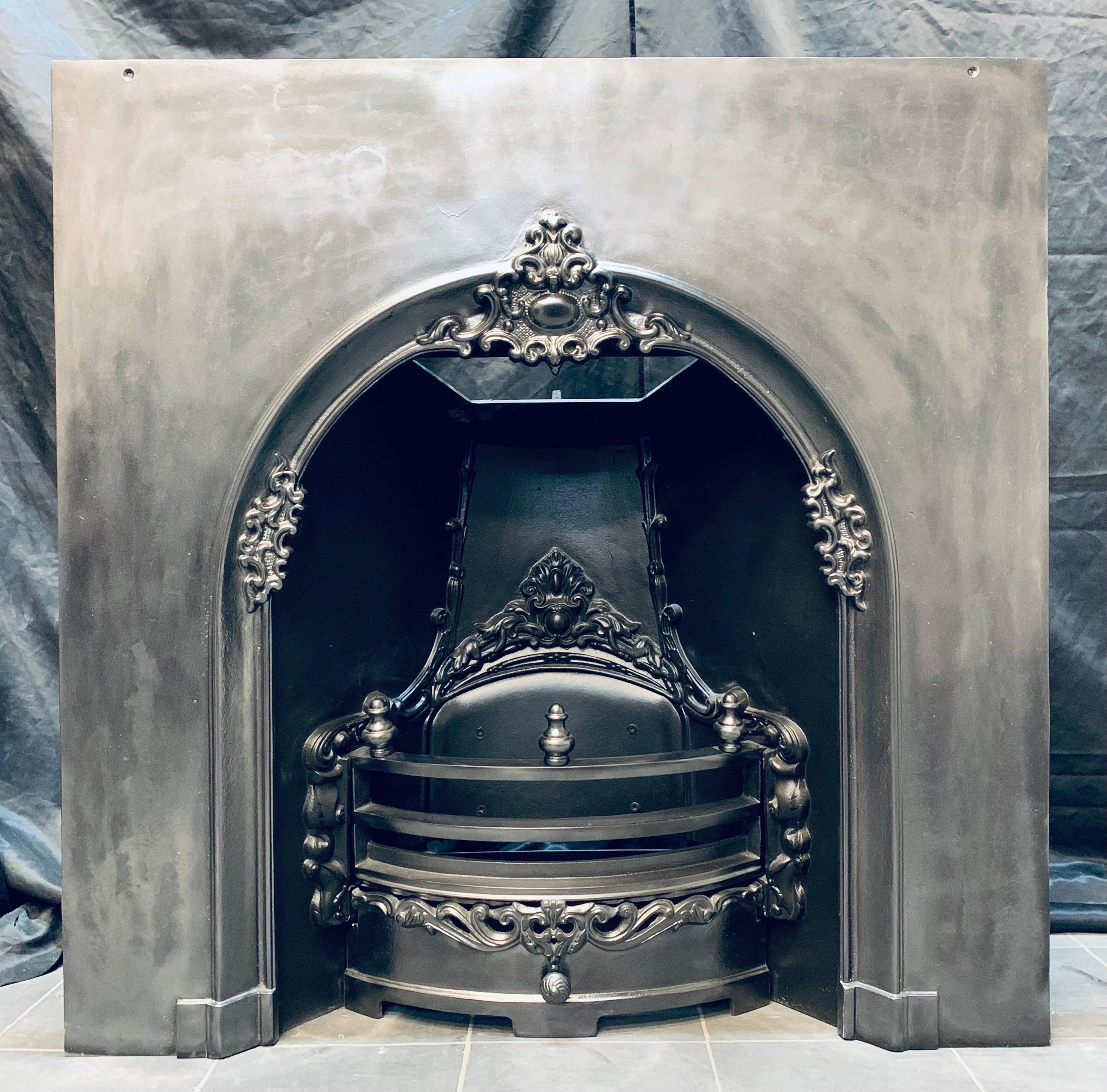 A large Victorian style cast iron arched fireplace insert with a central high relief cartouche, a generous outer plate, complete with its original bars and ash pan door, topped with finials and a funnel chamber back.