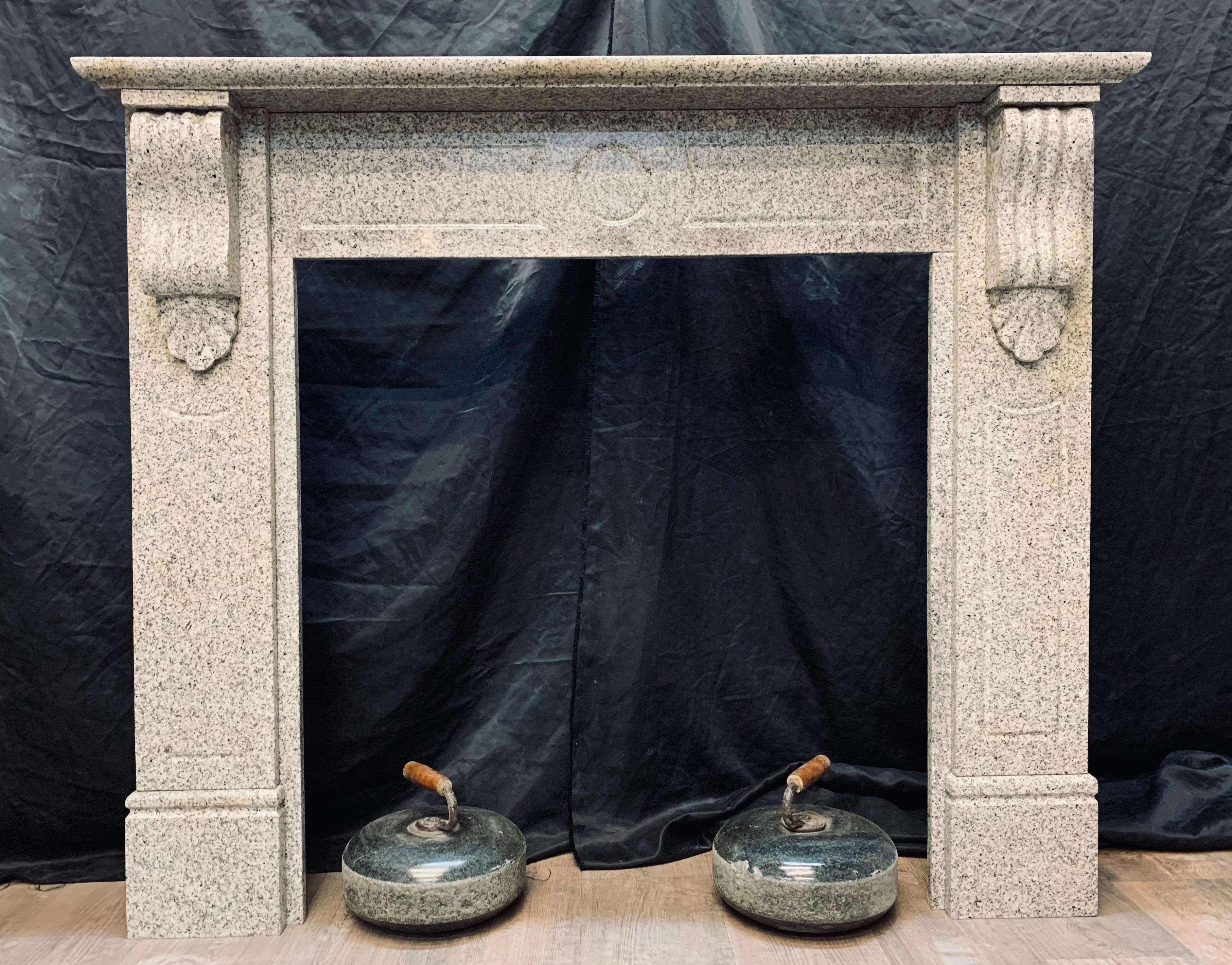 A stylish Victorian style carved Scottish Kenmay granite corbelled fireplace surround. A moulded top shelf sits above a frieze with fluted panels flanked by tall jambs displaying the same fluted design with shaped geometric corbels and shells, all