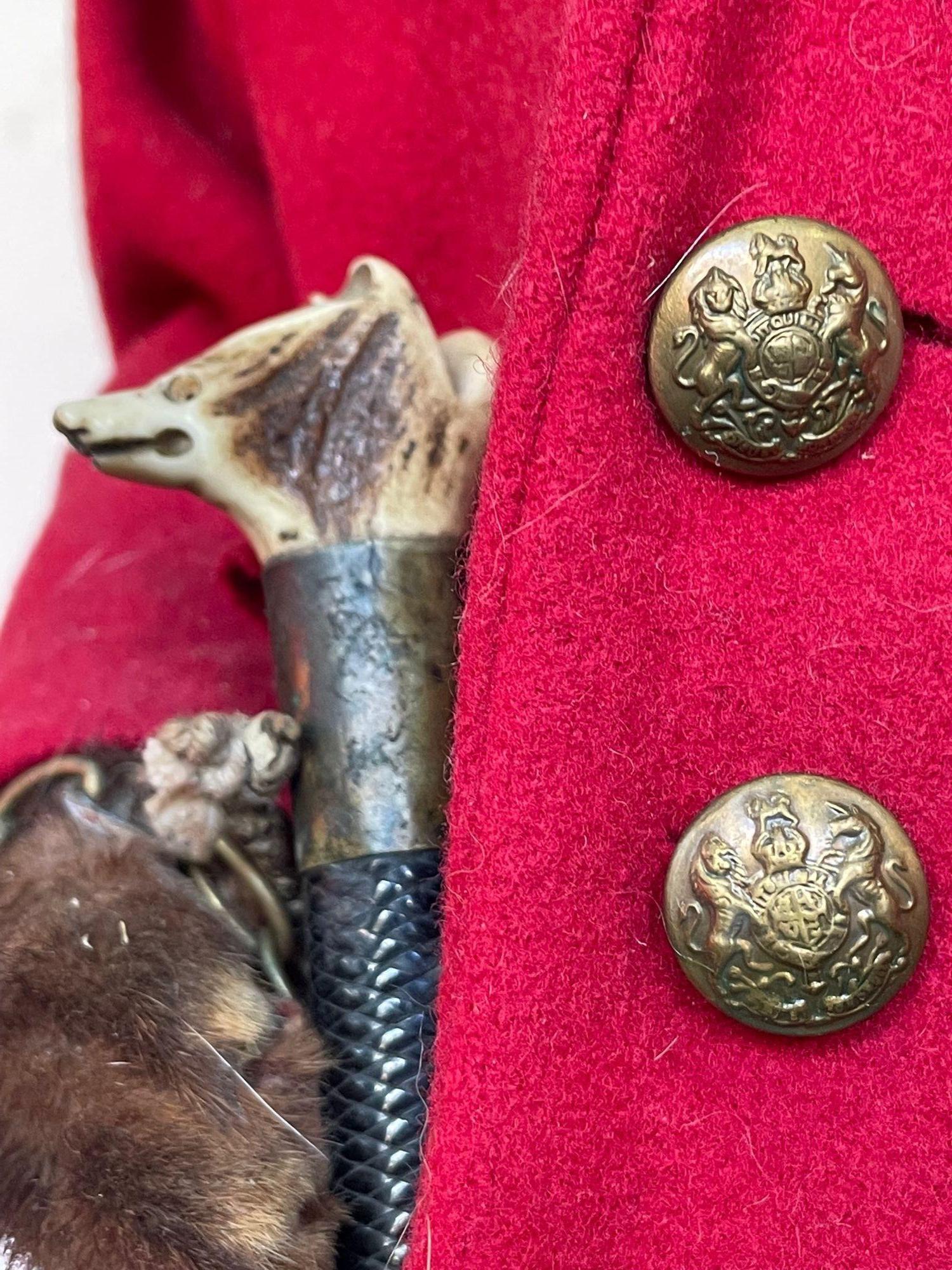 Un renard taxidermique victorien vêtu d'une tenue de chasse complète comprenant une veste de chasse rouge écarlate avec des boutons en laiton, des bottes d'équitation en cuir, des jodhpurs, une cravache en os sculptée en forme de tête de renard et