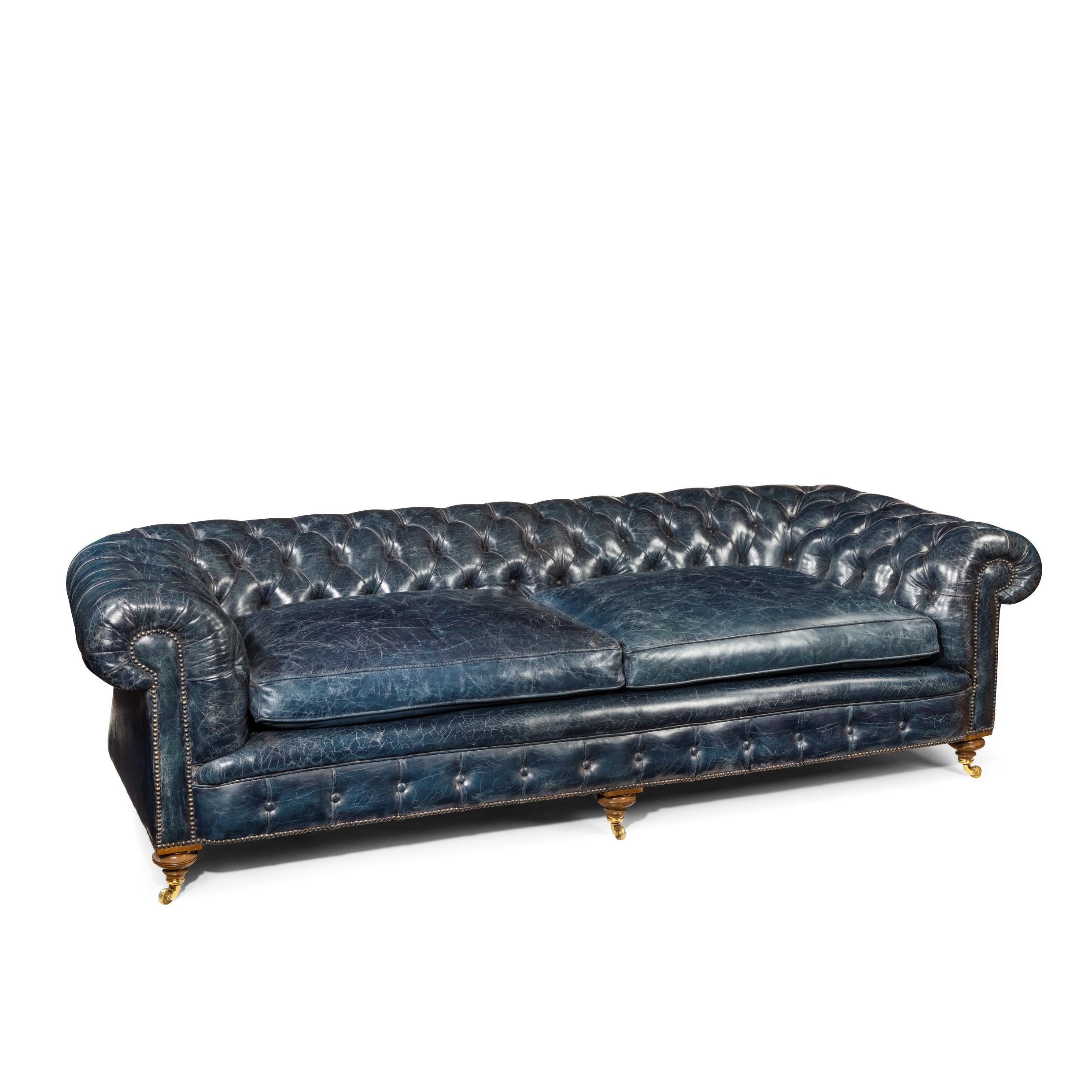 A Victorian three seater walnut chesterfield sofa, of typical form with rolled arms and two seat cushions, on turned and reeded legs with the original castors, reupholstered in deep-buttoned and distressed blue leather. English,