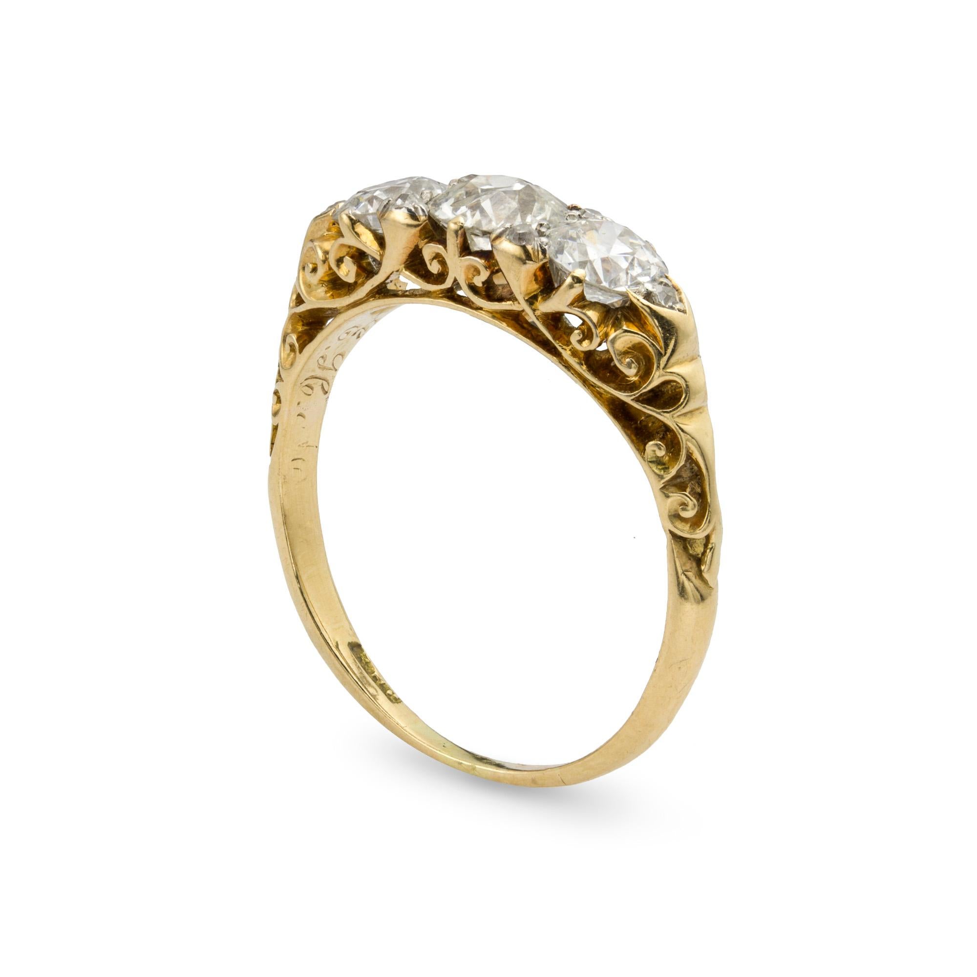 A Victorian three stone diamond ring, set with three old brilliant-cut diamonds, estimated total diamond weight 1.5 carats, set with rose-cut diamonds, all on an 14ct yellow gold carved mount, circa 1880, the head measuring 0.6x1.9 cm, gross weight