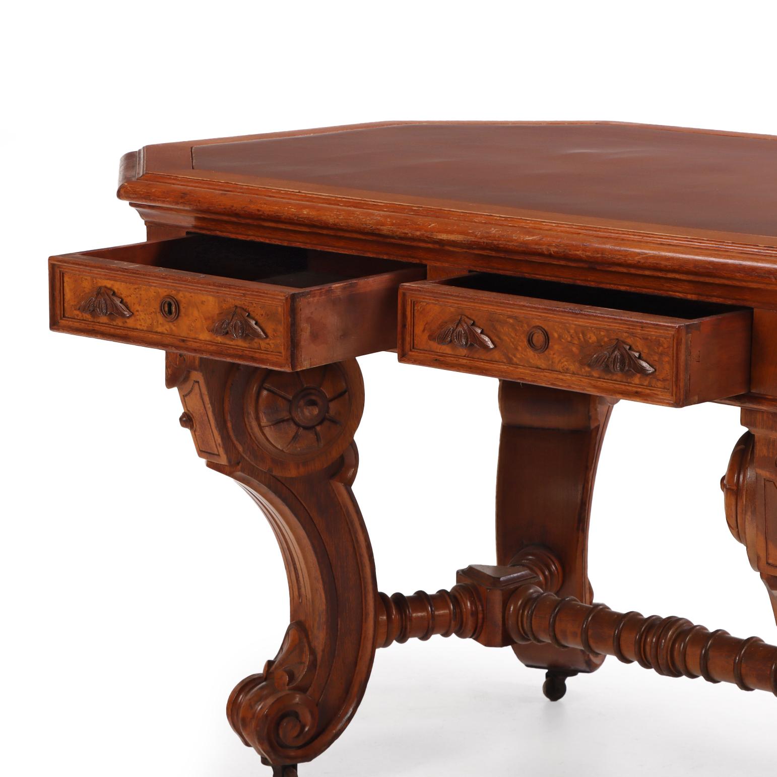 Dieser massive Schreibtisch im Renaissance-Revival-Stil verfügt über eine geformte Platte mit eingelassener Schreibfläche aus Kunstleder und zwei Schubladen auf jeder Seite. Das Möbelstück ruht auf geschnitzten, geschwungenen Beinen, die durch eine