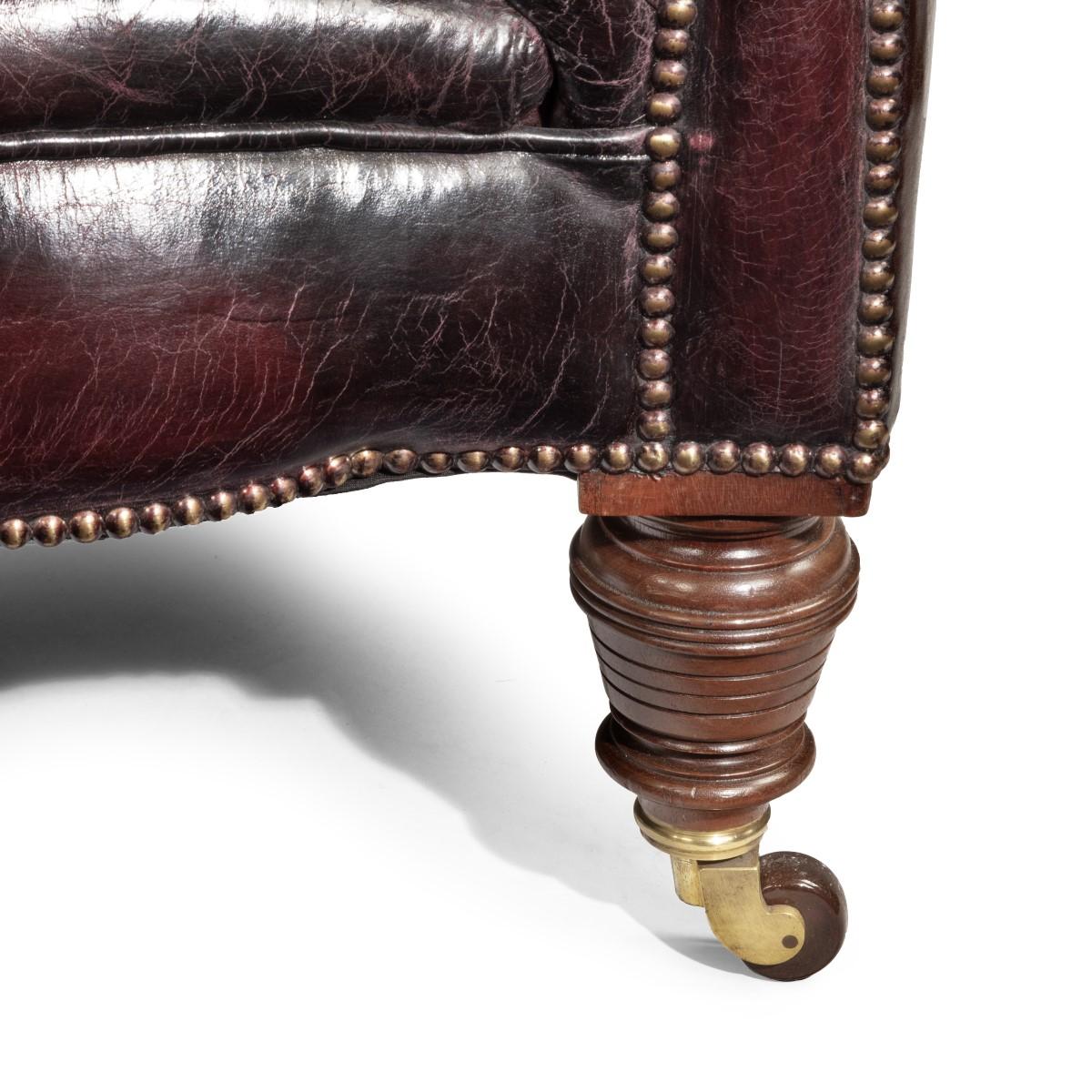 Divano Chesterfield vittoriano in noce, dalla tipica forma con braccioli arrotolati e due cuscini di seduta, con gambe anteriori e posteriori tornite e montate sulle rotelle originali, rivestito in pelle bordeaux con bottoni profondi e afflosciata.