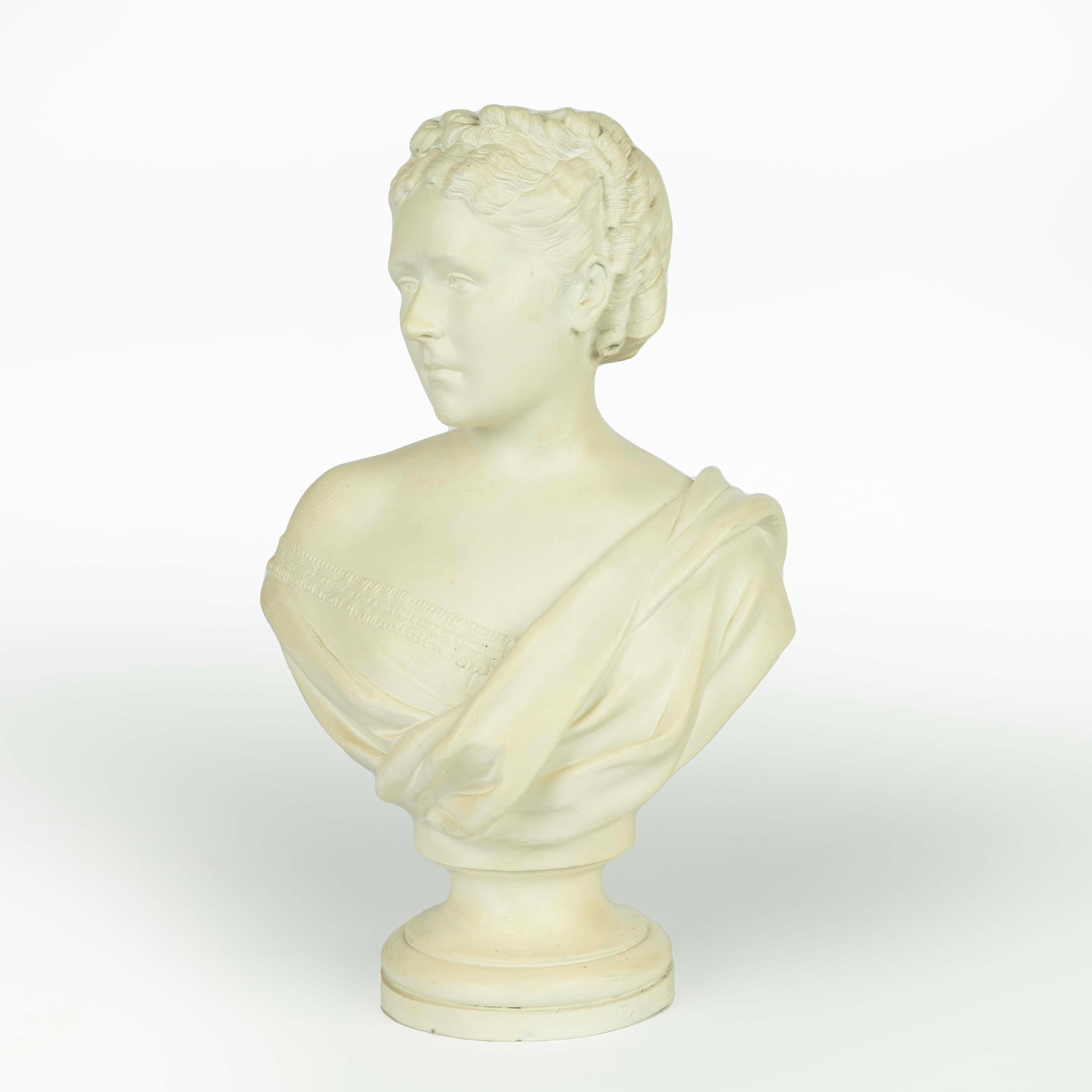 A Victorian white painted terracotta bust of a young woman, wearing a draped shawl over a bodice with a lace trim, her hair elaborately coiffed with a broad plait and multiple ringlets. English, circa 1860.