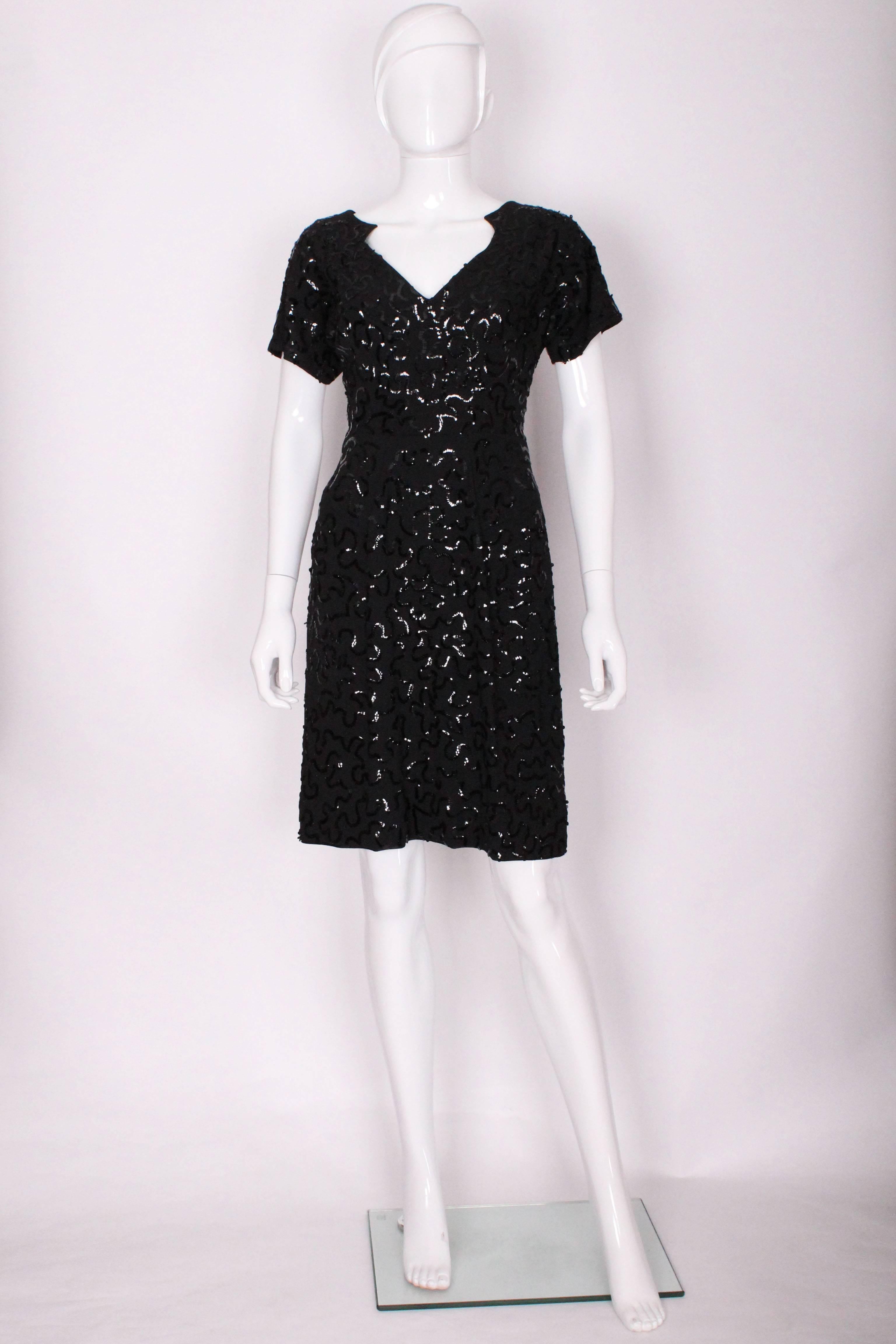 A chic cocktail dress by French designer Jeanne Paquin.
The dress is made of a wool crepe with black sequins sewn on in a squiggle pattern . It has a v neckline with shape at the shoulder and 'backline', with a central back zip.It has short sleaves,