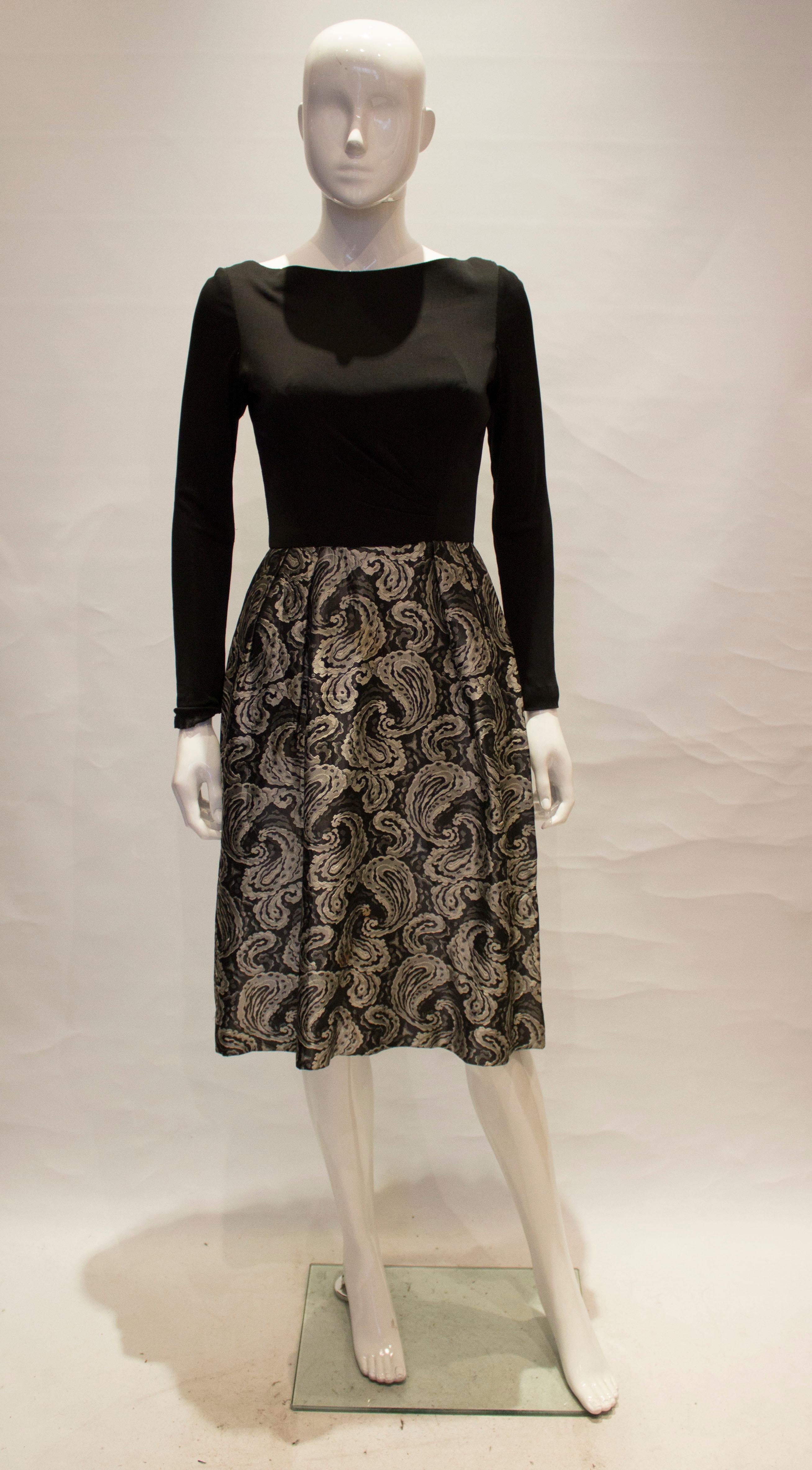 A lovely 1950s brocade dress with a black top and silver and black paisley printed skirt, it has a lovely low back and zips at the back 

measurements taken flat in inches are

bust - 16inches
waist - 13inches 
length - 42inches