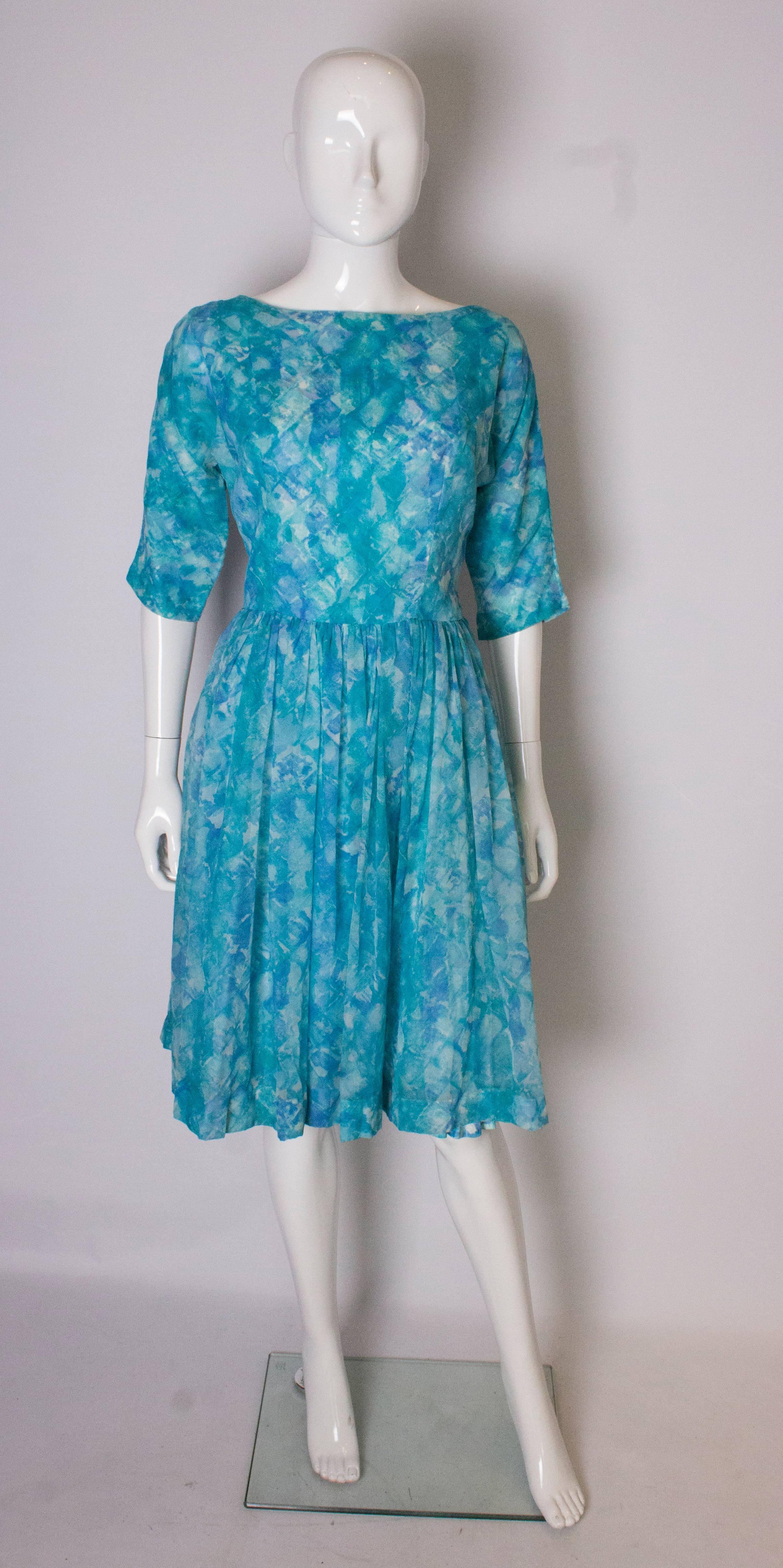 A great, vintage swing cinch cocktail  dress in multiple shades on blue. The dress has a printed underskirt in the same print as the over skirt, and  has a back central zip, elbow length sleaves, and belt hoops.