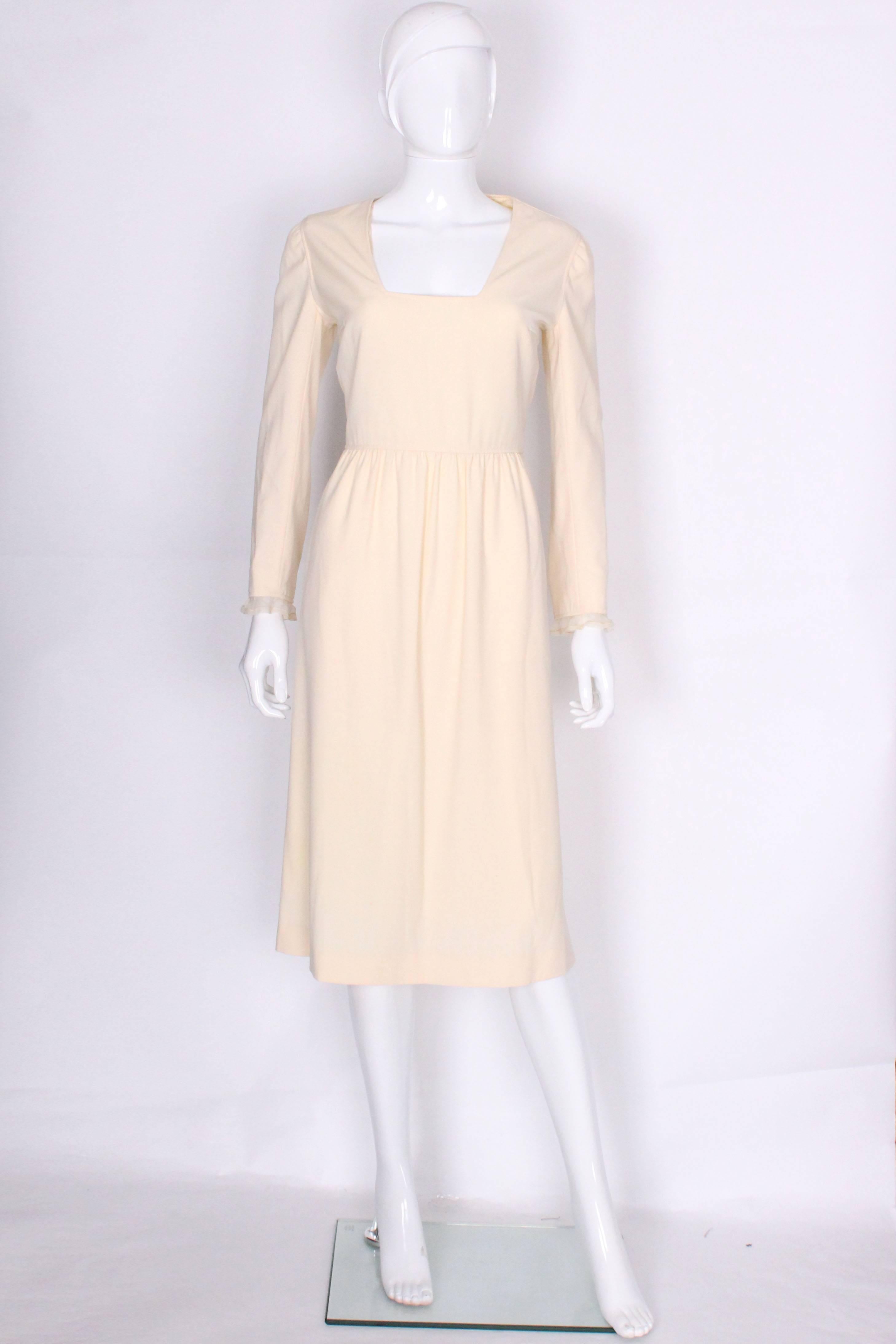 A chic dress by French designer Courreges. In a cream wool with silk lining, this dress is perfect for parties or  even a bride.The dress has a square neckline, a 7 button opening at the back and silk chiffon frills at the cuff. The seam work is