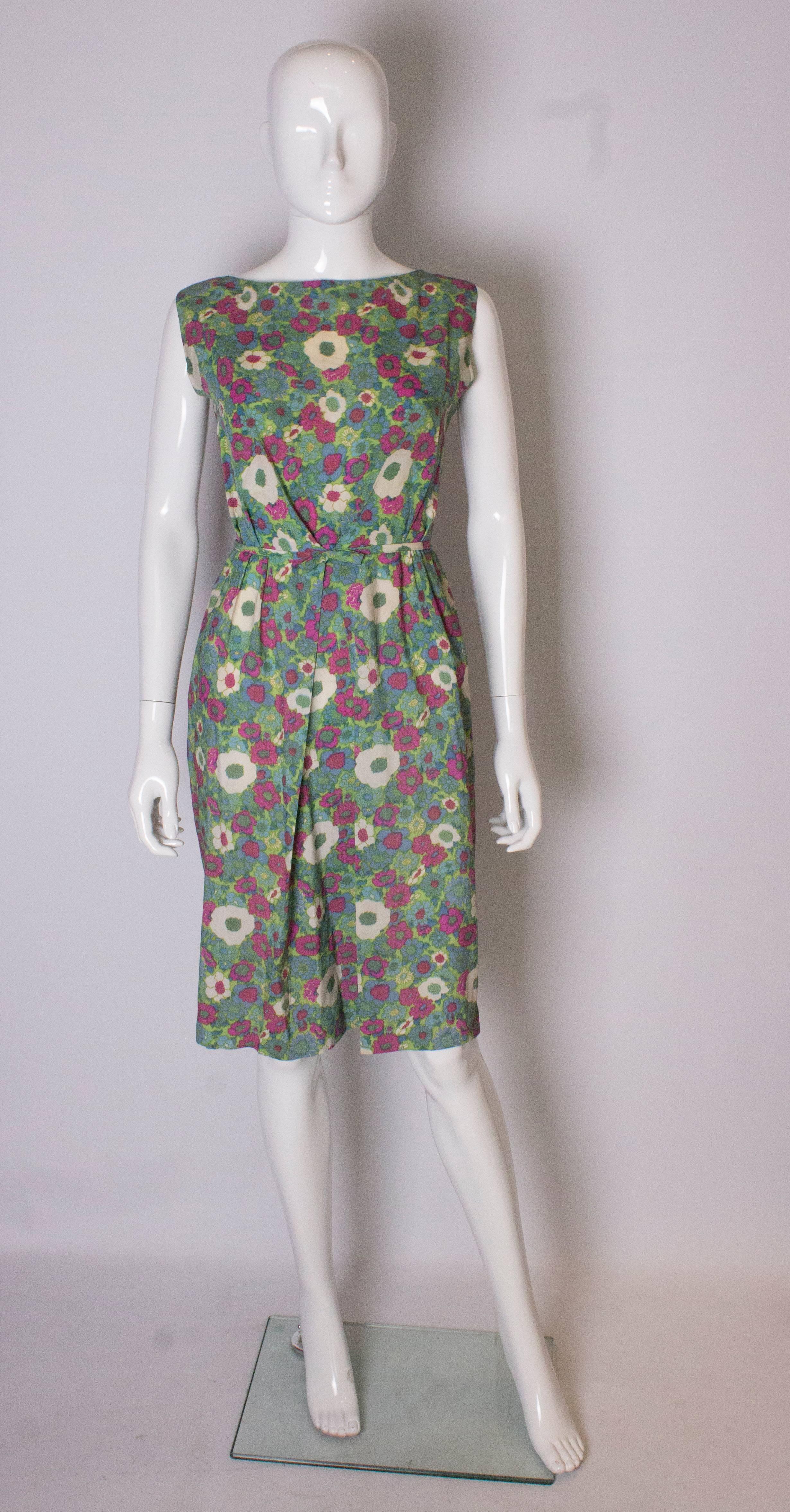 A pretty vintage dress for Spring/Summer, in a green, burgundy, blue and cream floral print. The dress has a pleat and gathering at the front with a  bow. It opens at the back with 5 buttons and 3 poppers.