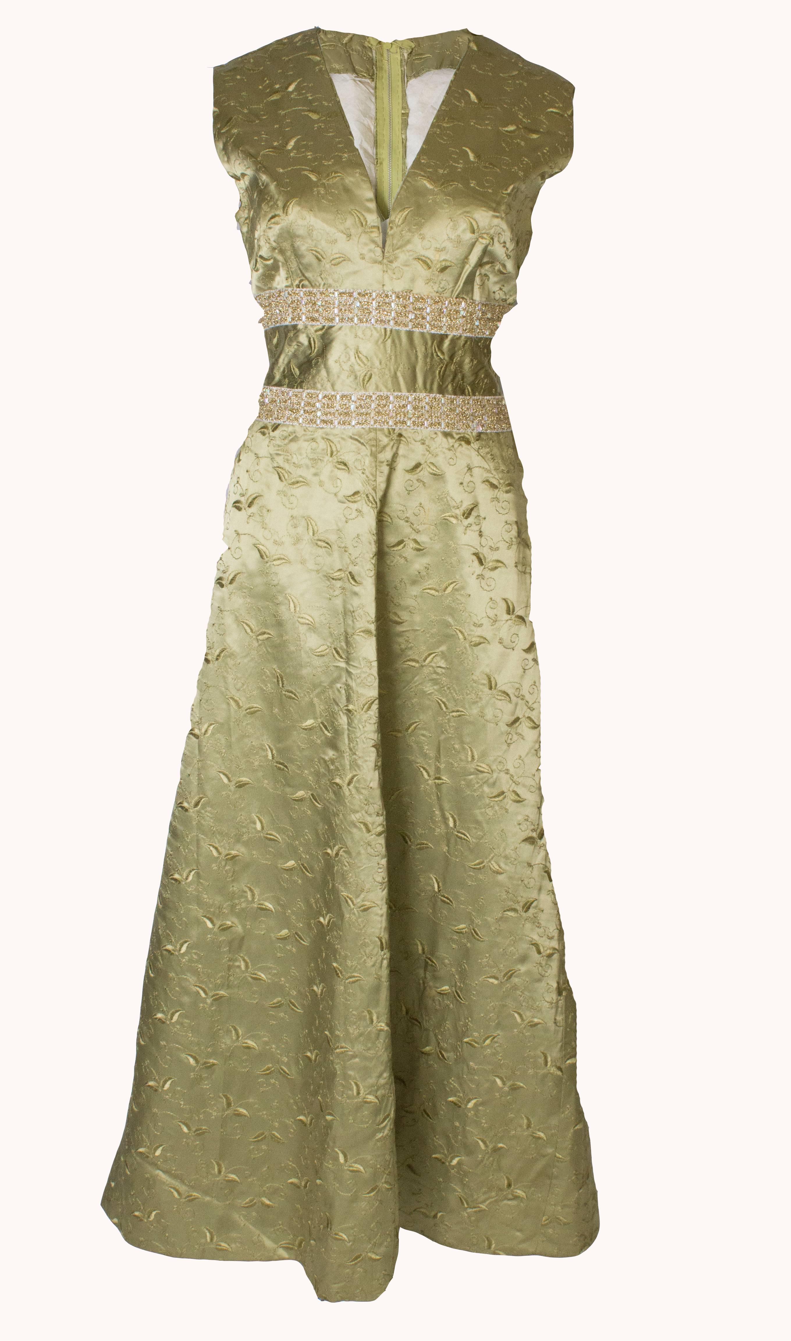 An elegant sage green vintage gown from the 1960s  in a silk mix fabric with embroidery.  The vintage dress  is  sleaveless and has a v neckline, central back zip and two rows of detail.
