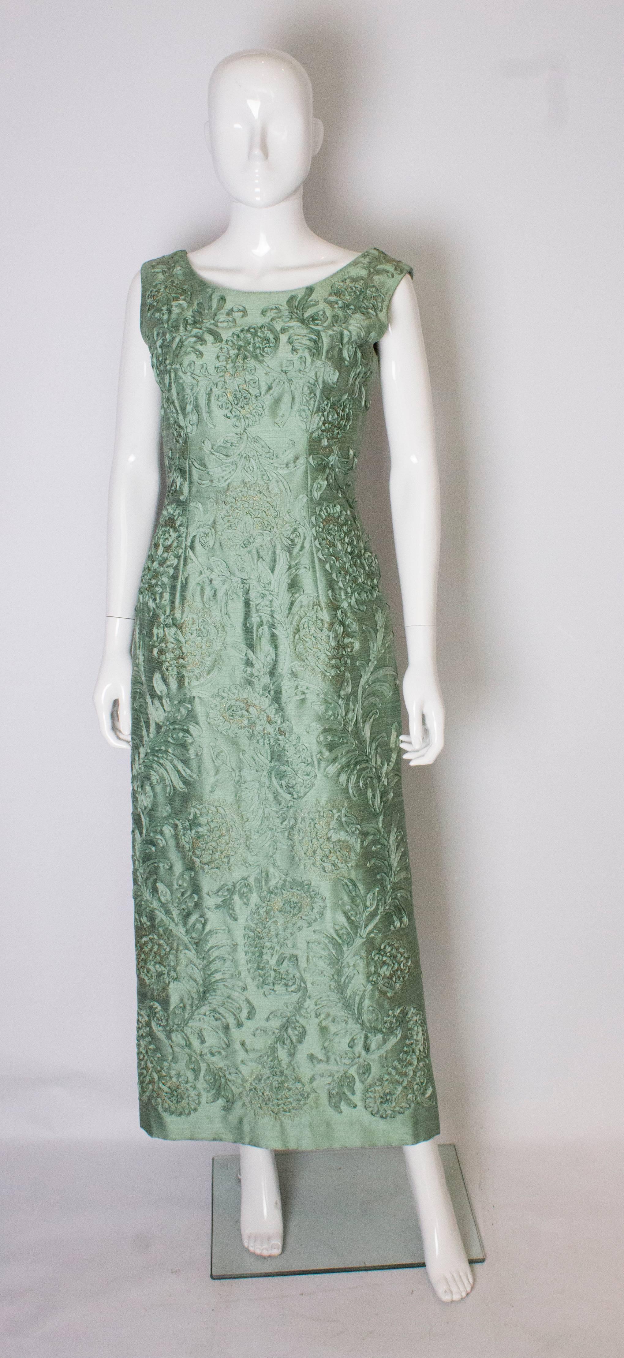 A chic vintage sage green evening gown by Carita Couture . The dress is made of a sage green fabric, speckled with gold and has ribbon decoration.
The dress has a scoop back and front with a  central back zip, and a 15'' slit at the back.