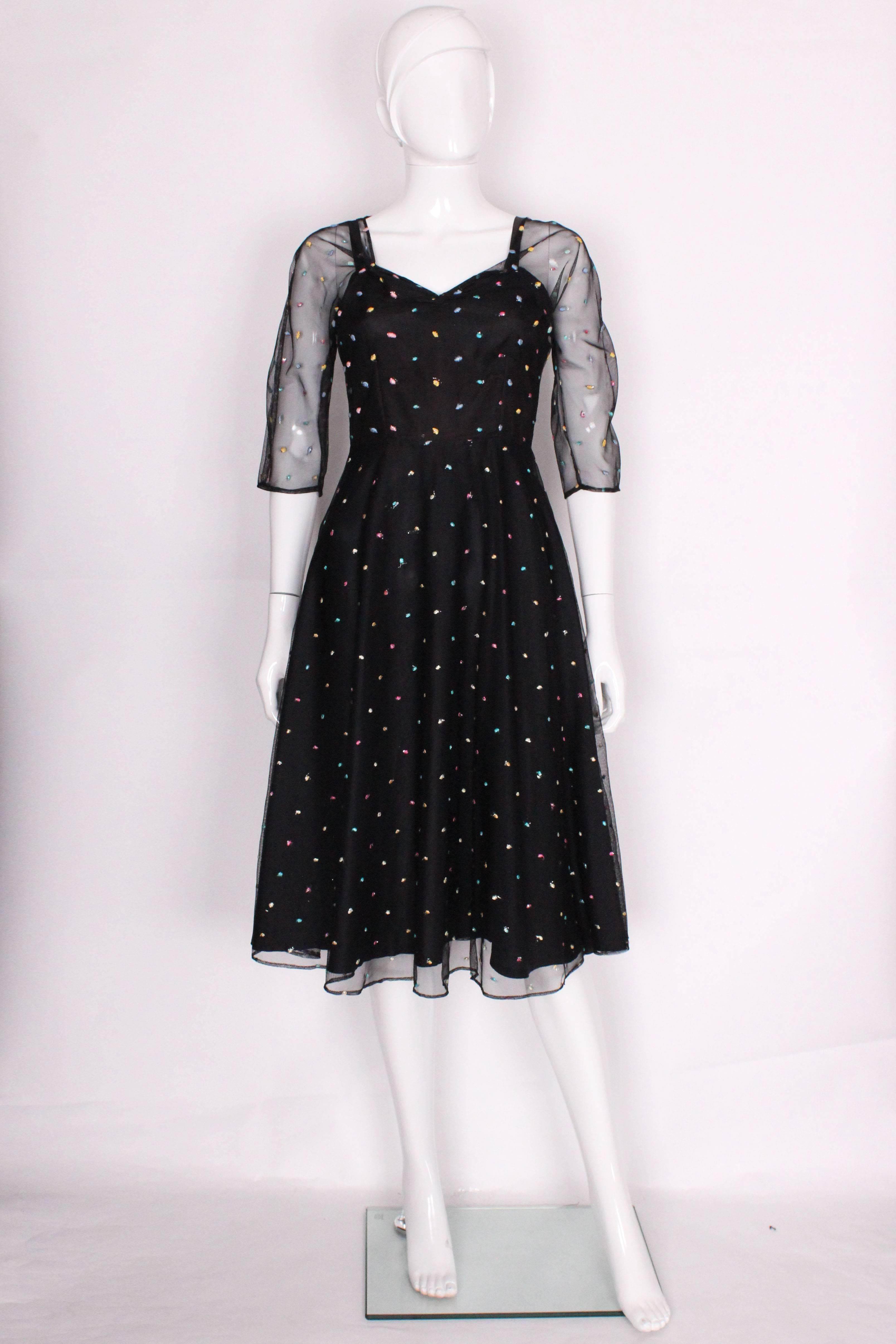 A great party dress by Radley. The dress has an underdress in black , overlayed in black net with sewn spots in many colours. It has elbow length sleeves, a sweetheart neckline, and central back zip.