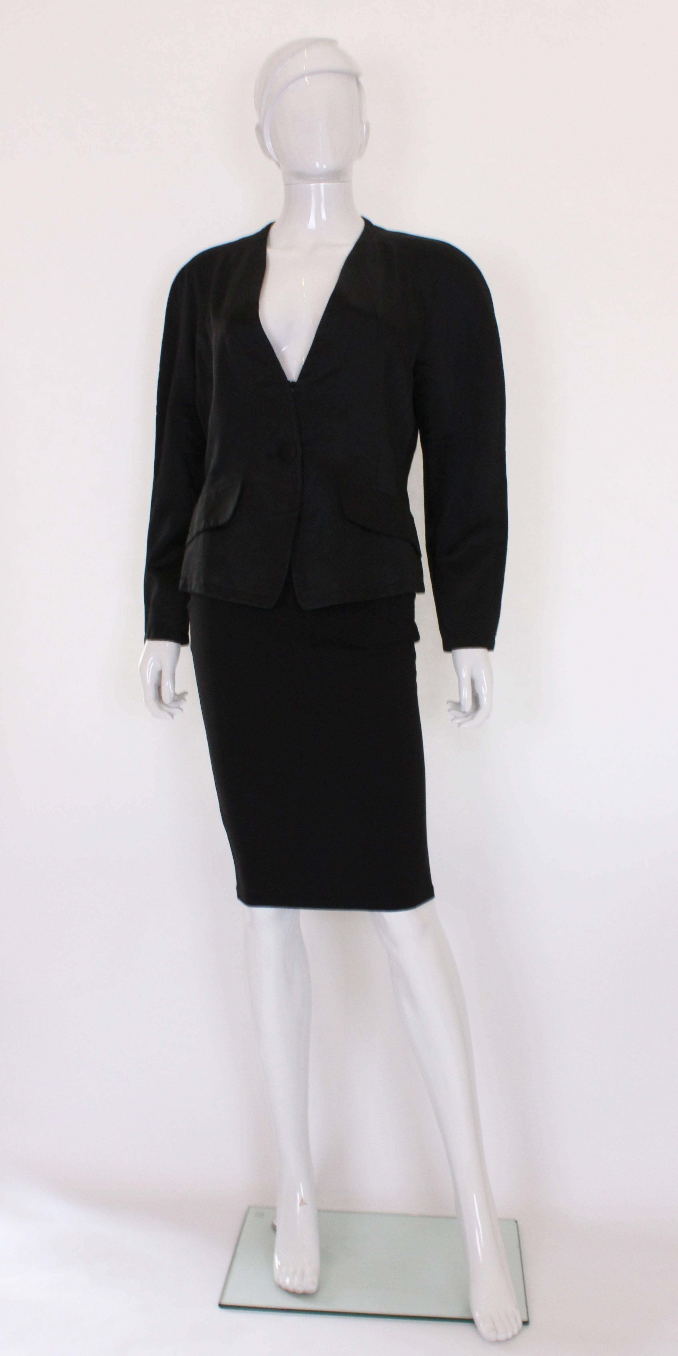 A great black evening jacket from Yves Saint Laurent , Variation line.
This jacket has soft shoulders, is collarless with a v neckline and has a central button and ribbon fastening.