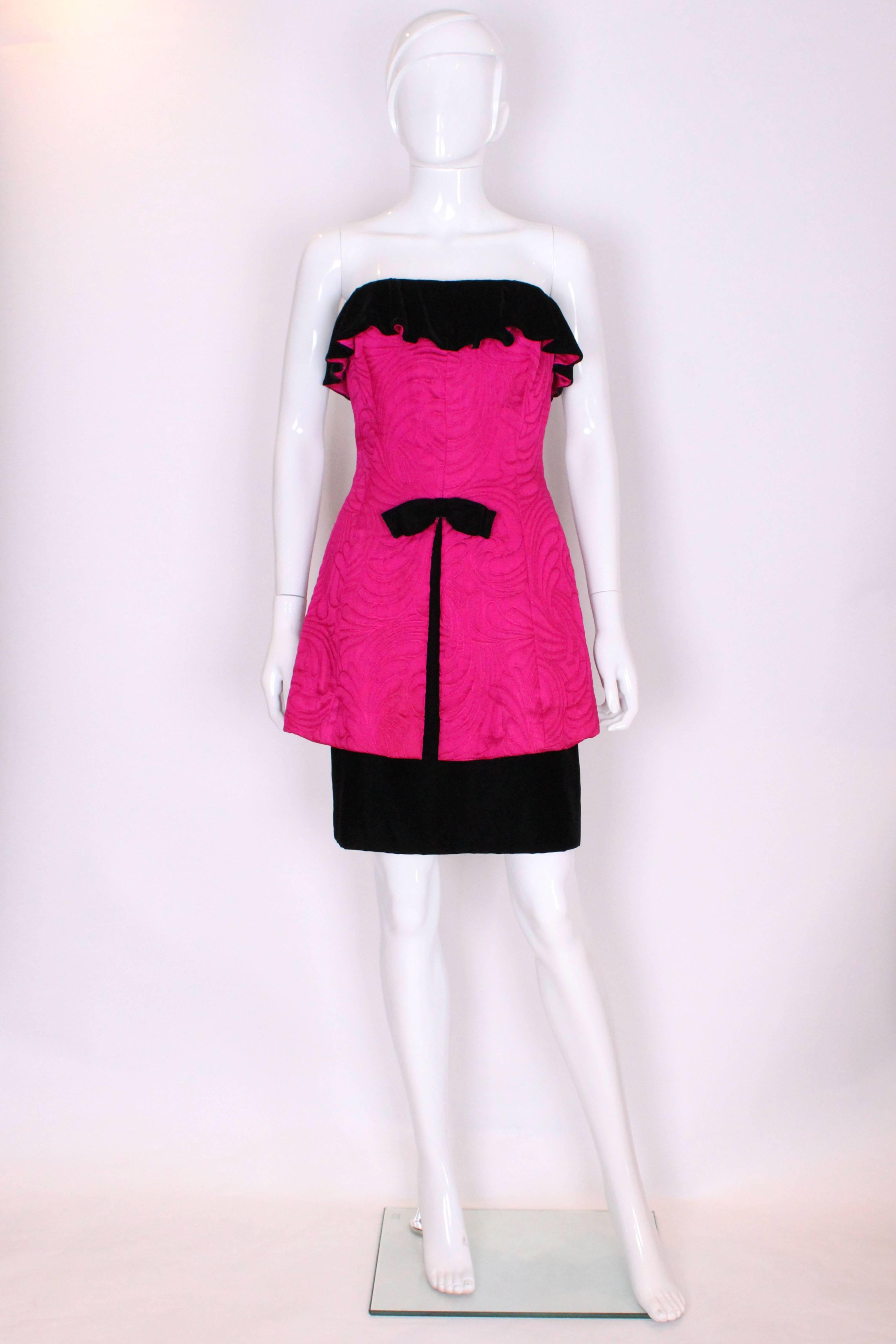 A real head turner for the party season. This dress is a wonderful shade of shocking pink , in a quilted fabric on the outer layer , with a black velvet under skirt, fold over top and bow.