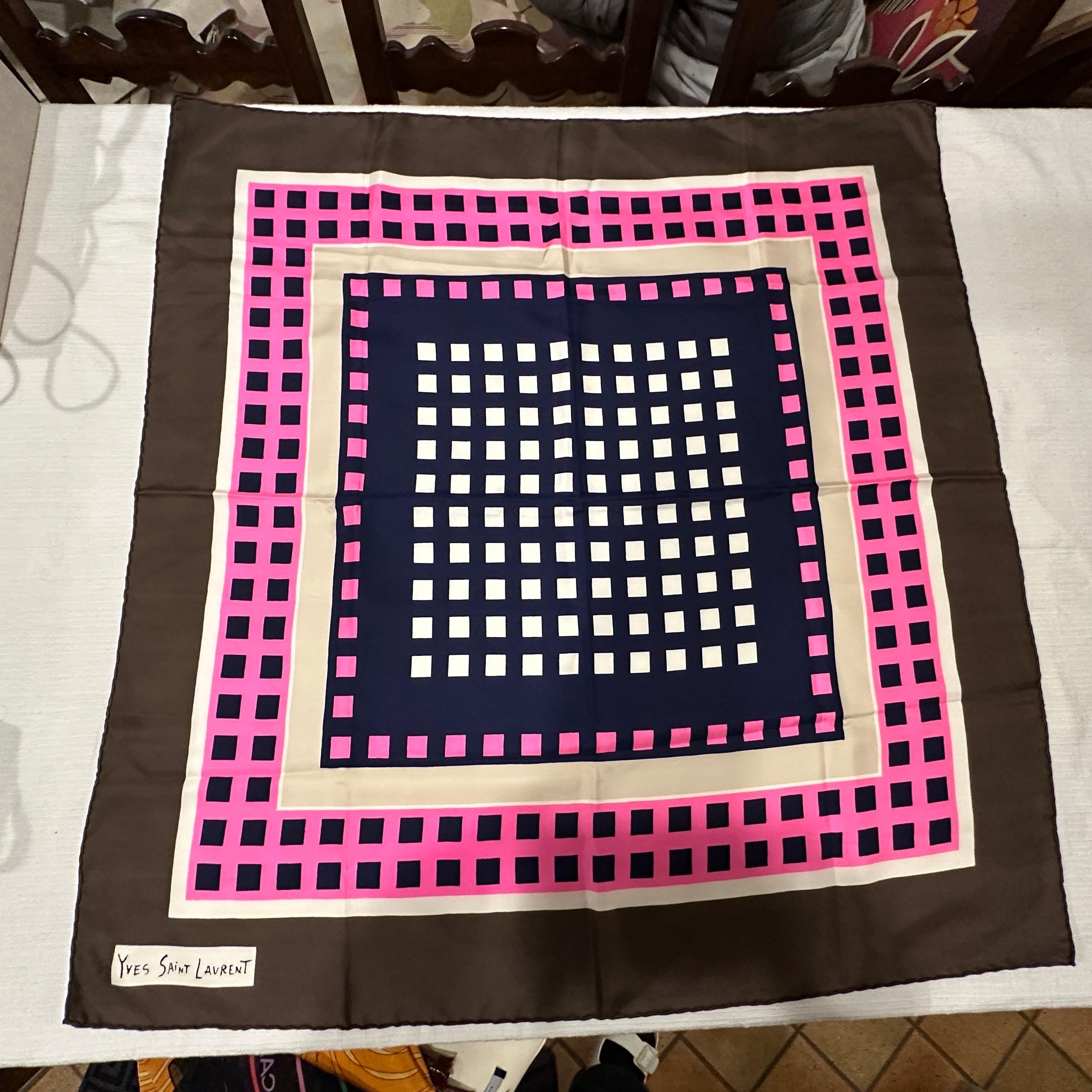 This is a vintage Yves Saint Laurent geometric silk scarf from the 1980s. It features a bold and striking design composed of a square pattern, with alternating rows of dark navy, cream, and pink squares arranged symmetrically. The scarf's border