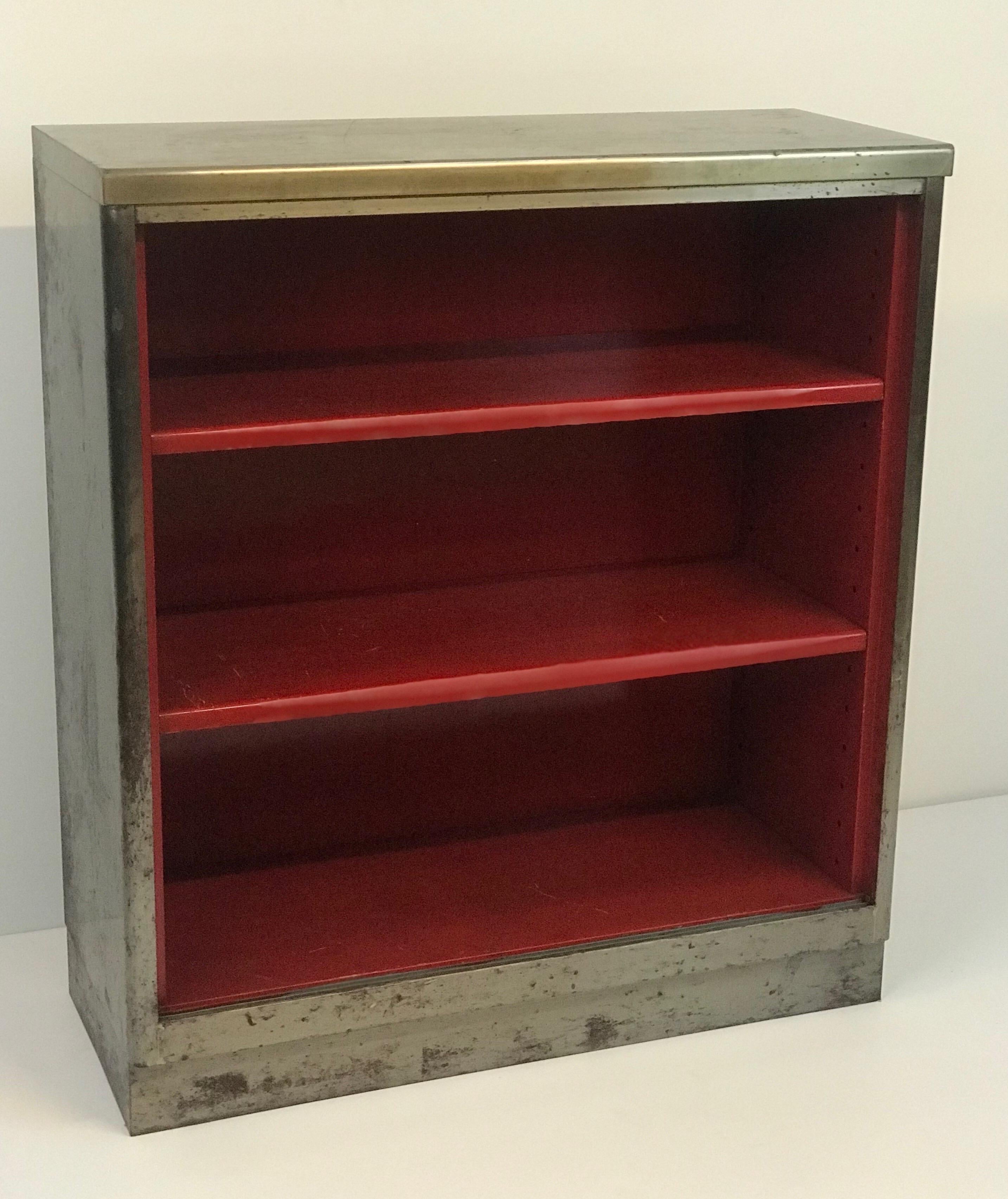 A 1960's Brushed steel bookcase with an interior painted in heavy automotive grade red paint. Made by Art Metal inc of Jamestown NY in a neutral or industrial color scheme the piece was likely stripped in the 1990's when the brushed steel look was