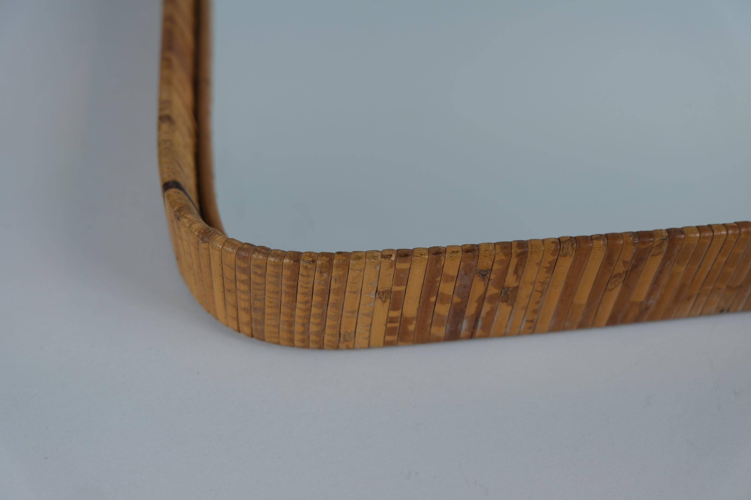 Un bellissimo specchio da parete con una splendida patina vintage sulla cornice in rattan e sulla superficie dello specchio. Questo pezzo risale agli anni '50-'60 ed è in condizioni assolutamente originali. Poiché non è timbrata, è quasi impossibile